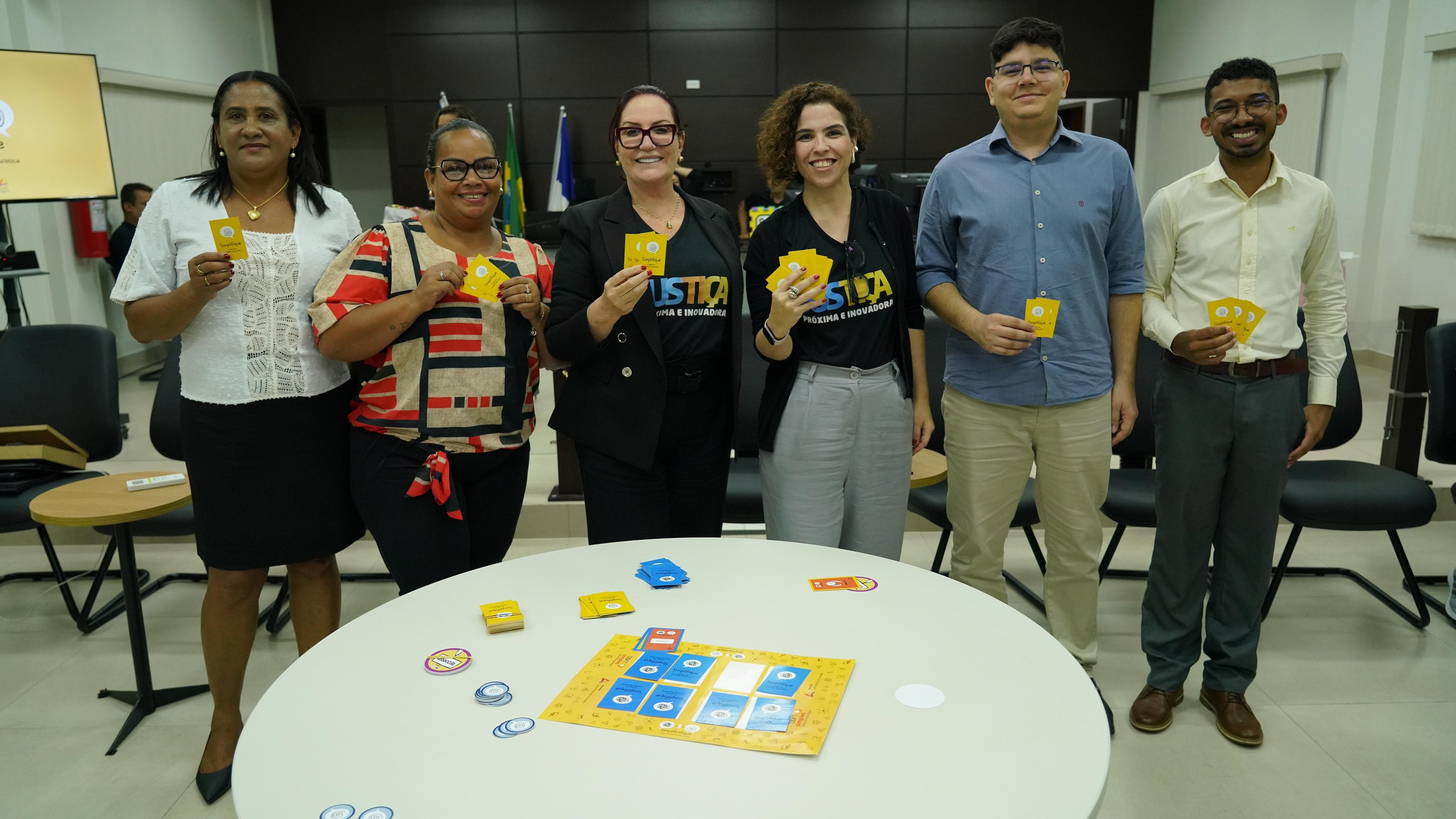 Homens e mulheres em foto posada numa sala de paredes laterais brancas e parede de madeira ao fundo