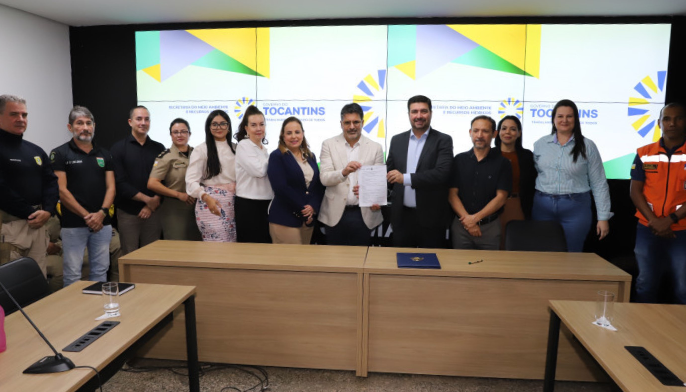 Fotografia colorida que mostra pessoas em pé segurando um documento