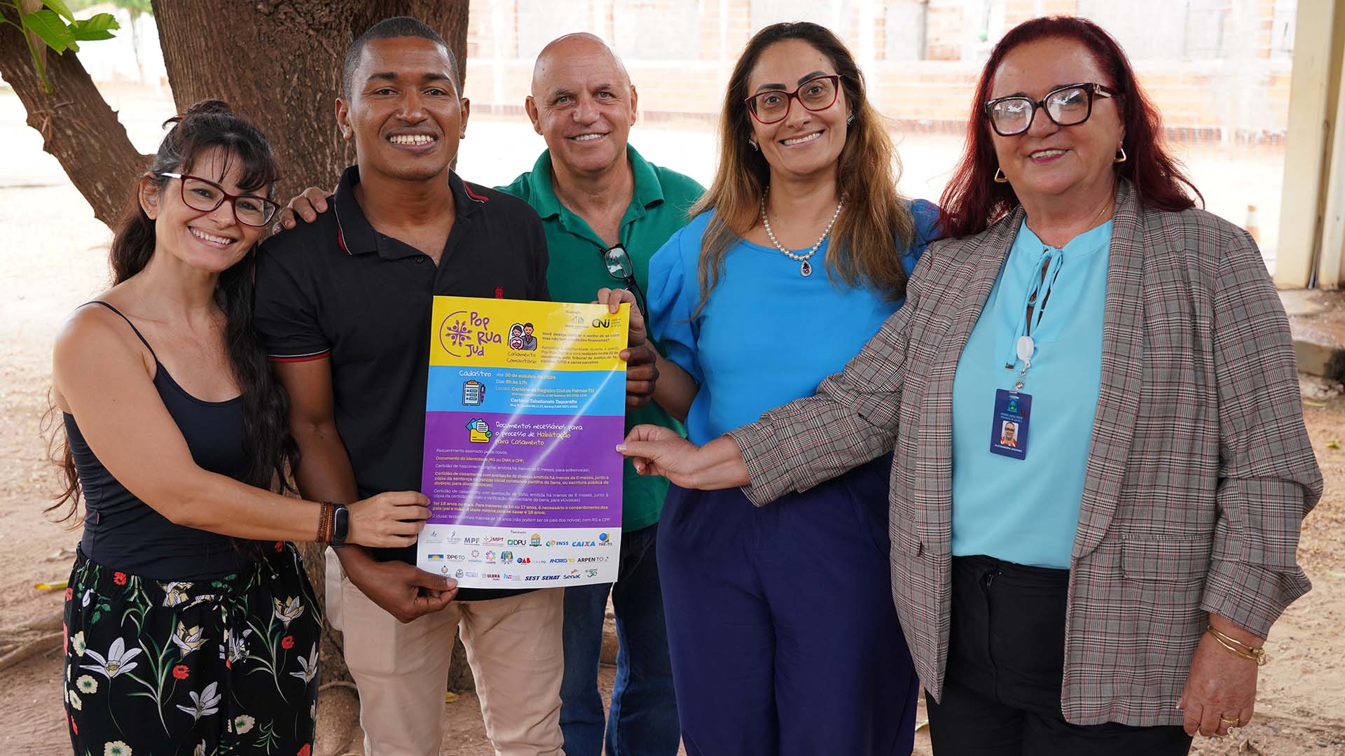 Imagem mostra cinco pessoas com roupas de várias cores, em pé, segurando um cartaz