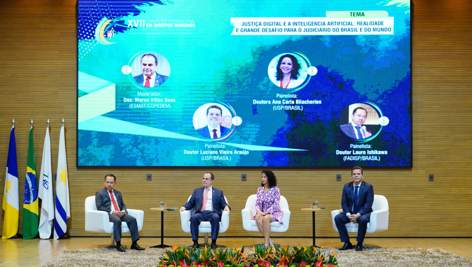 Fotografia colorida que mostra três homens e uma mulher sentados em um palco cujo fundo tem um telão azul com o tema do Congresso Internacional de Direitos humanos