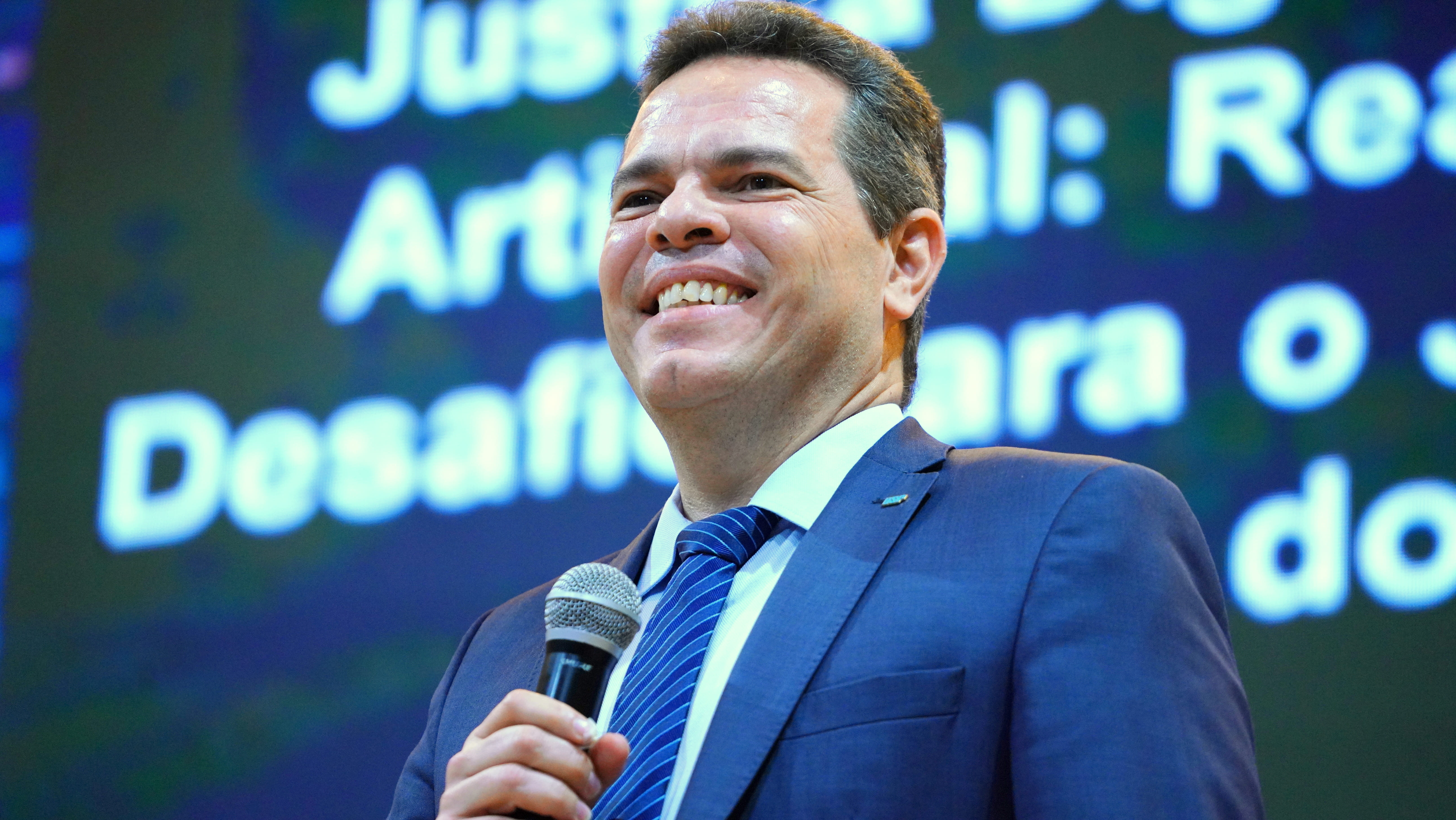 Fotografia colorida que mostra um homem branco de terno, sorrindo 