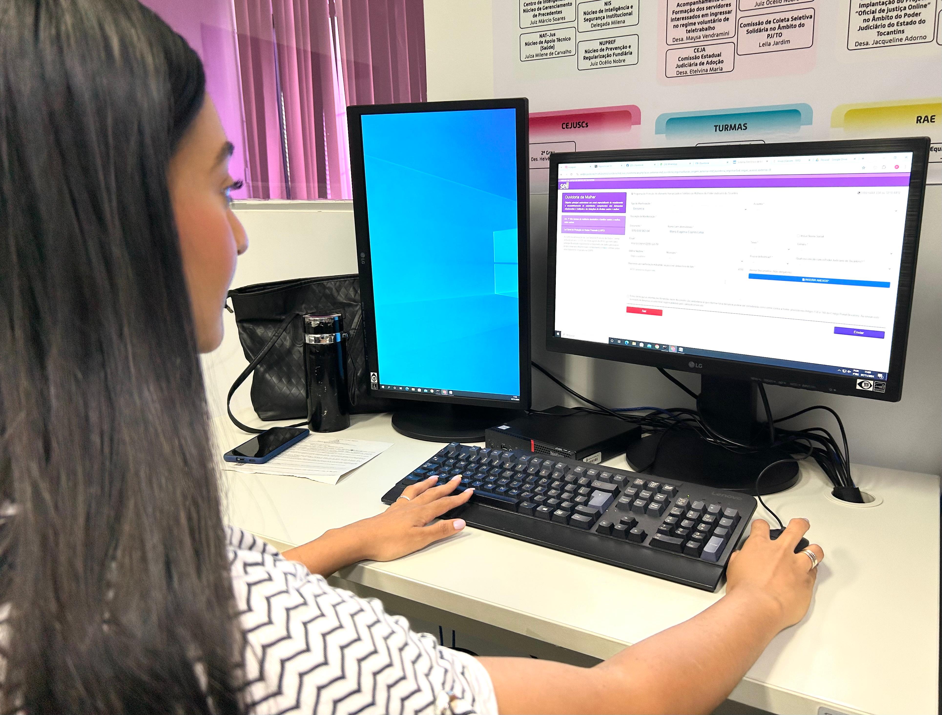 Fotografia colorida de uma mulher morena de cabelos longos usando o computador
