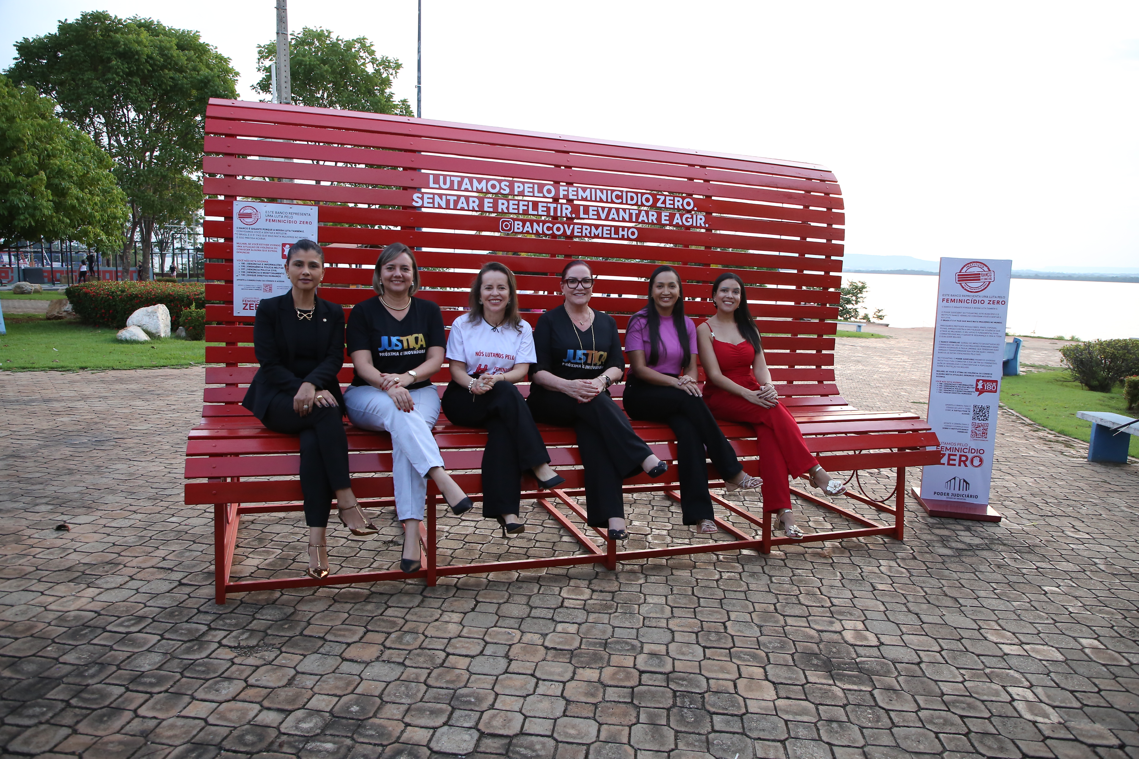 foto colorida horizontal mostra seis mulheres sentadas em um gigantesco banco vermelho ao fundo há arvores e as margens do rio tocantins 
