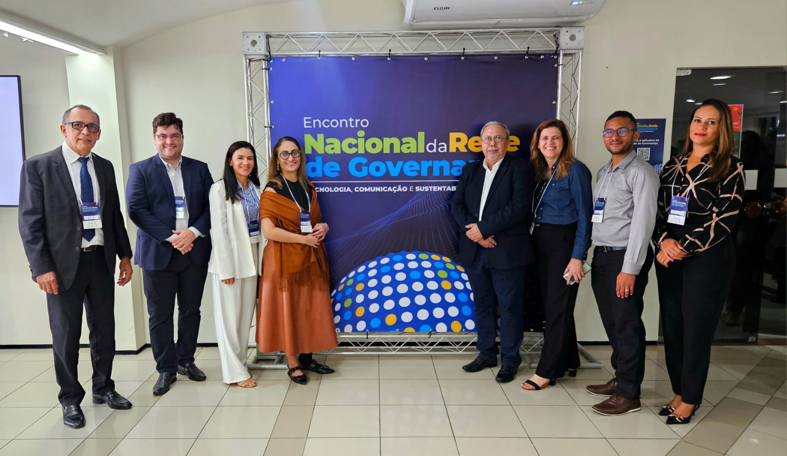 Pessoas estão em pé posando para foto atrás um banner do evento de governança