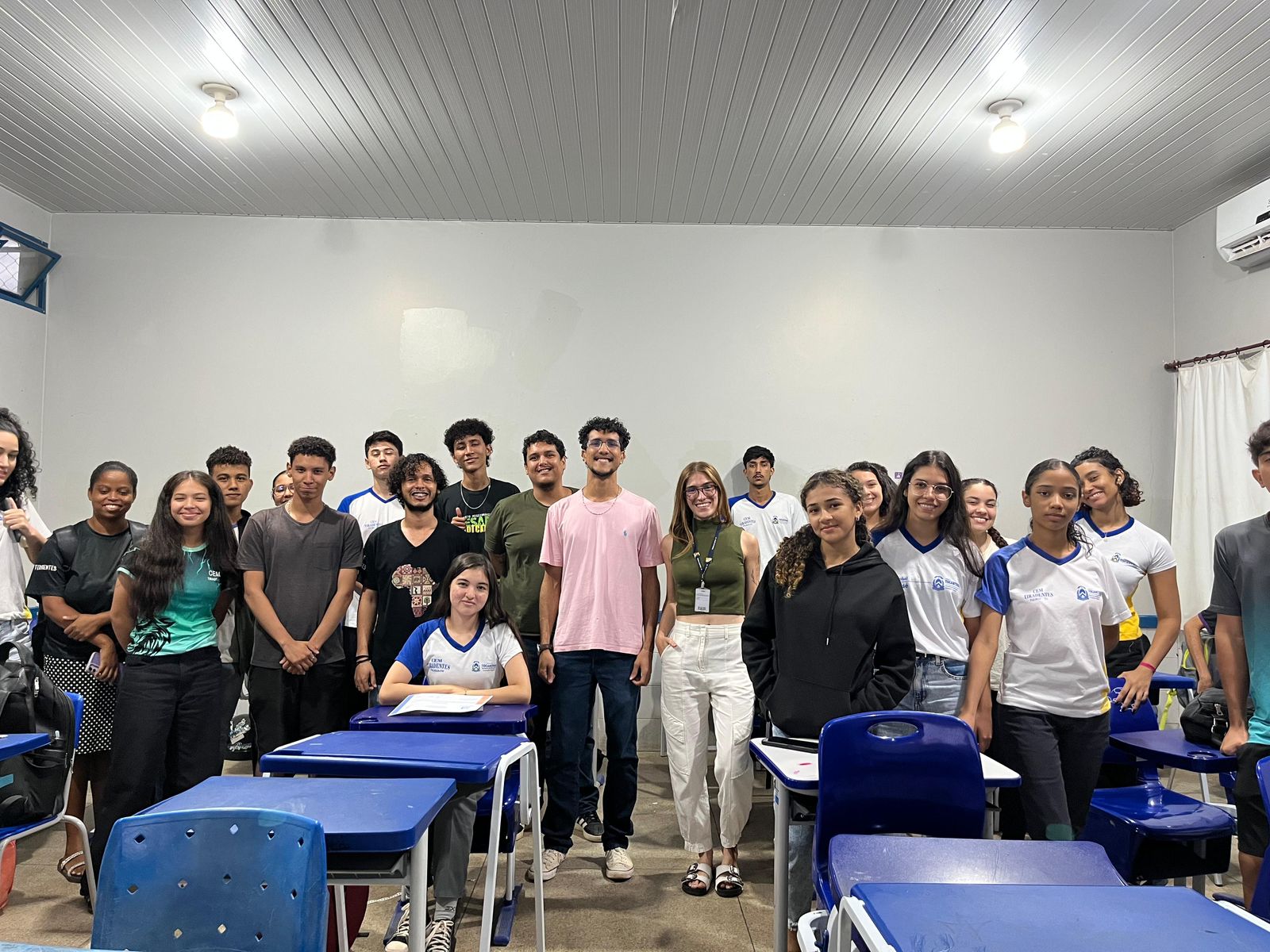 Fotografia colorida que mostra alunos e os palestrantes em uma mesma sala, posando para foto.