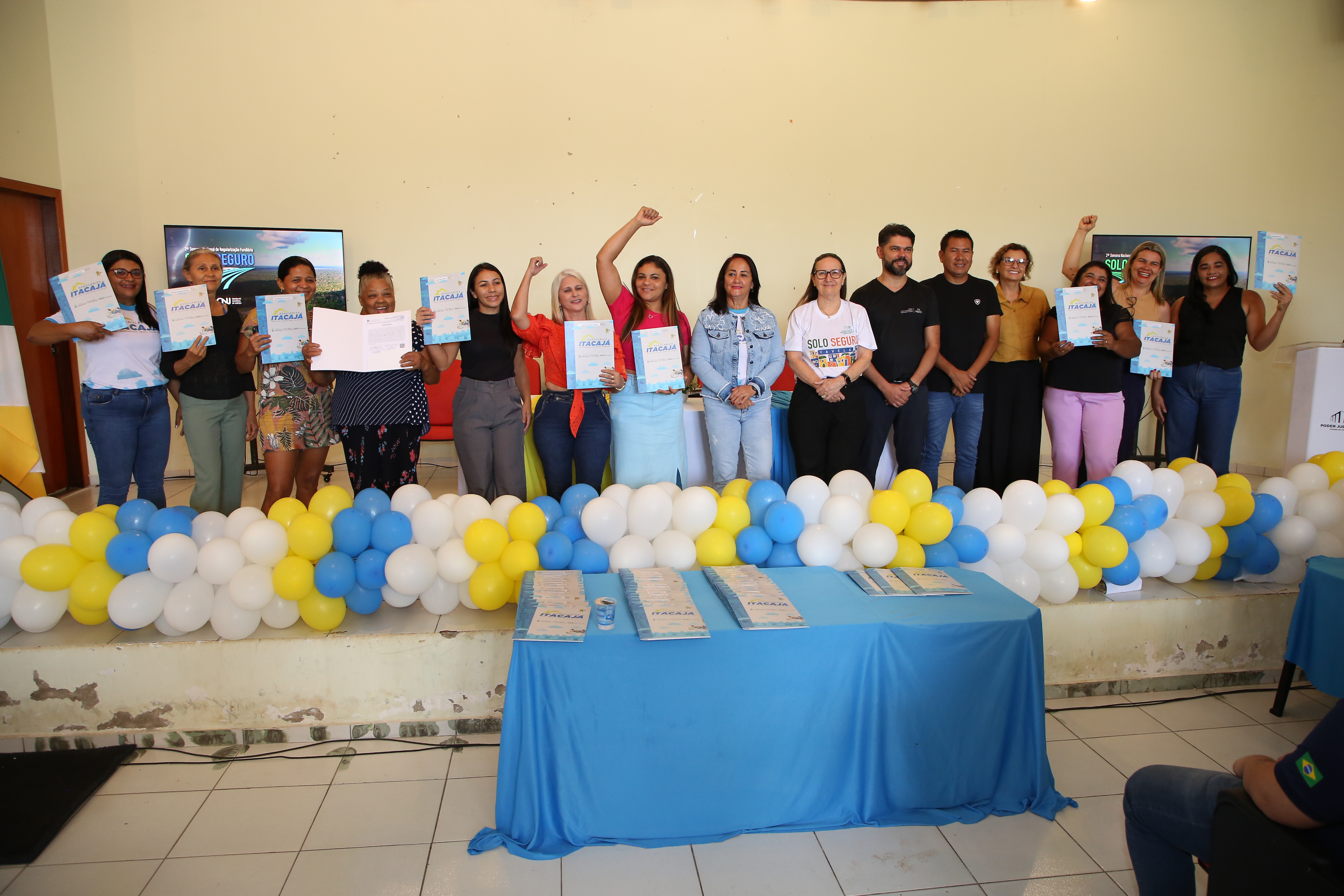 Fotografia colorida que mostra homens e mulheres felizes posando pra fotos com os braços erguidos