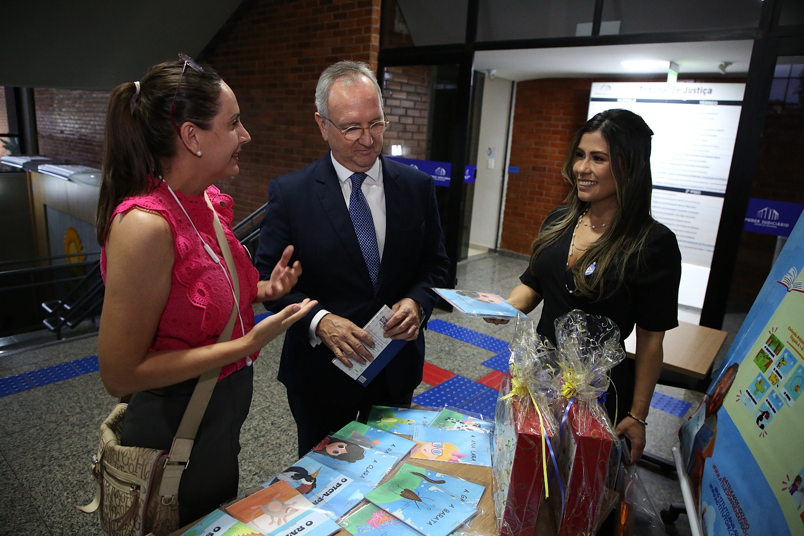 Desembargador Pedro Nelson com terno azul e duas mulheres estão olhando livros