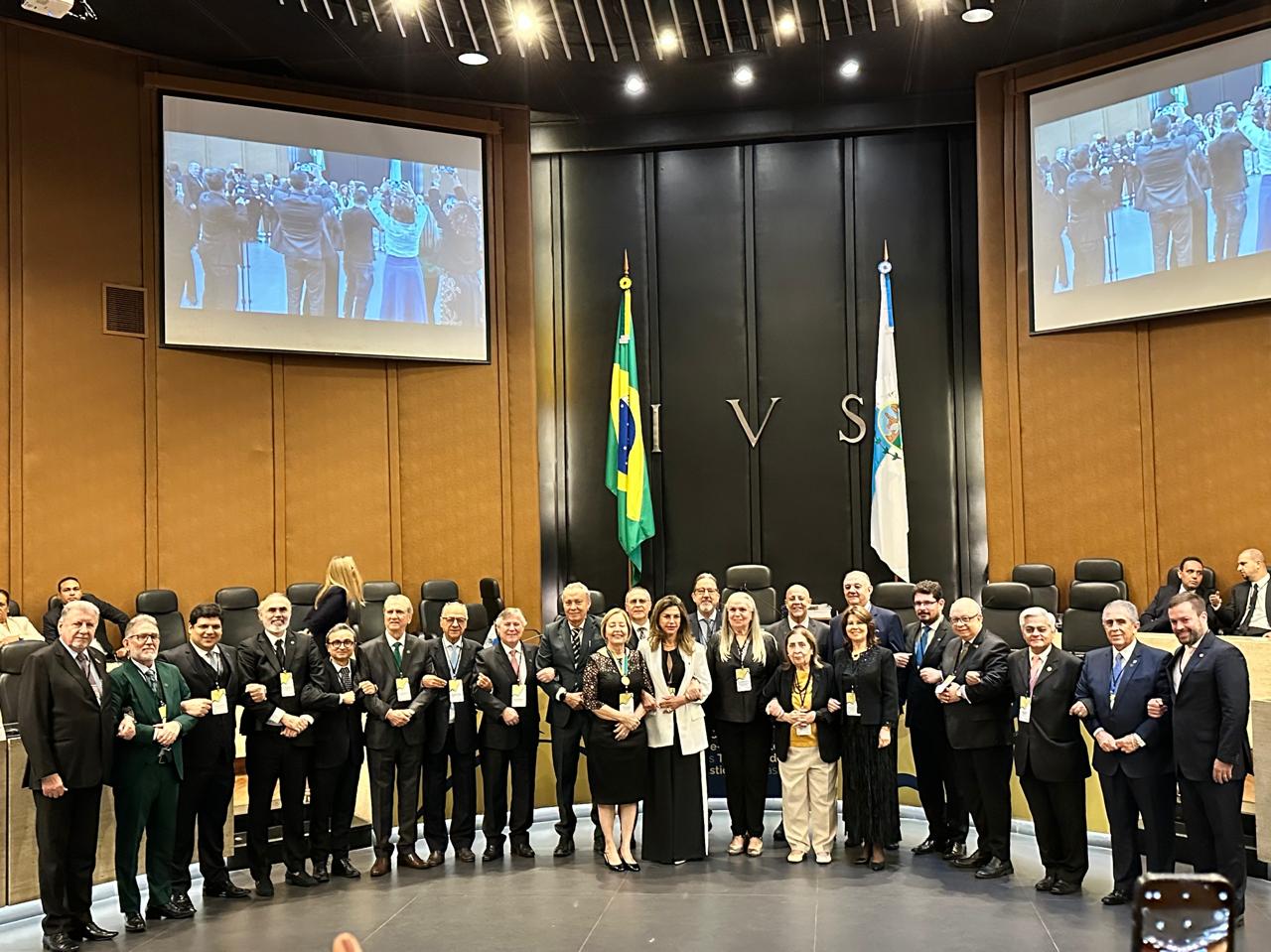 Fotografia colorida que mostra pessoas em pé, posando para a foto em frente às bandeiras do Brasil e do Rio de Janeiro