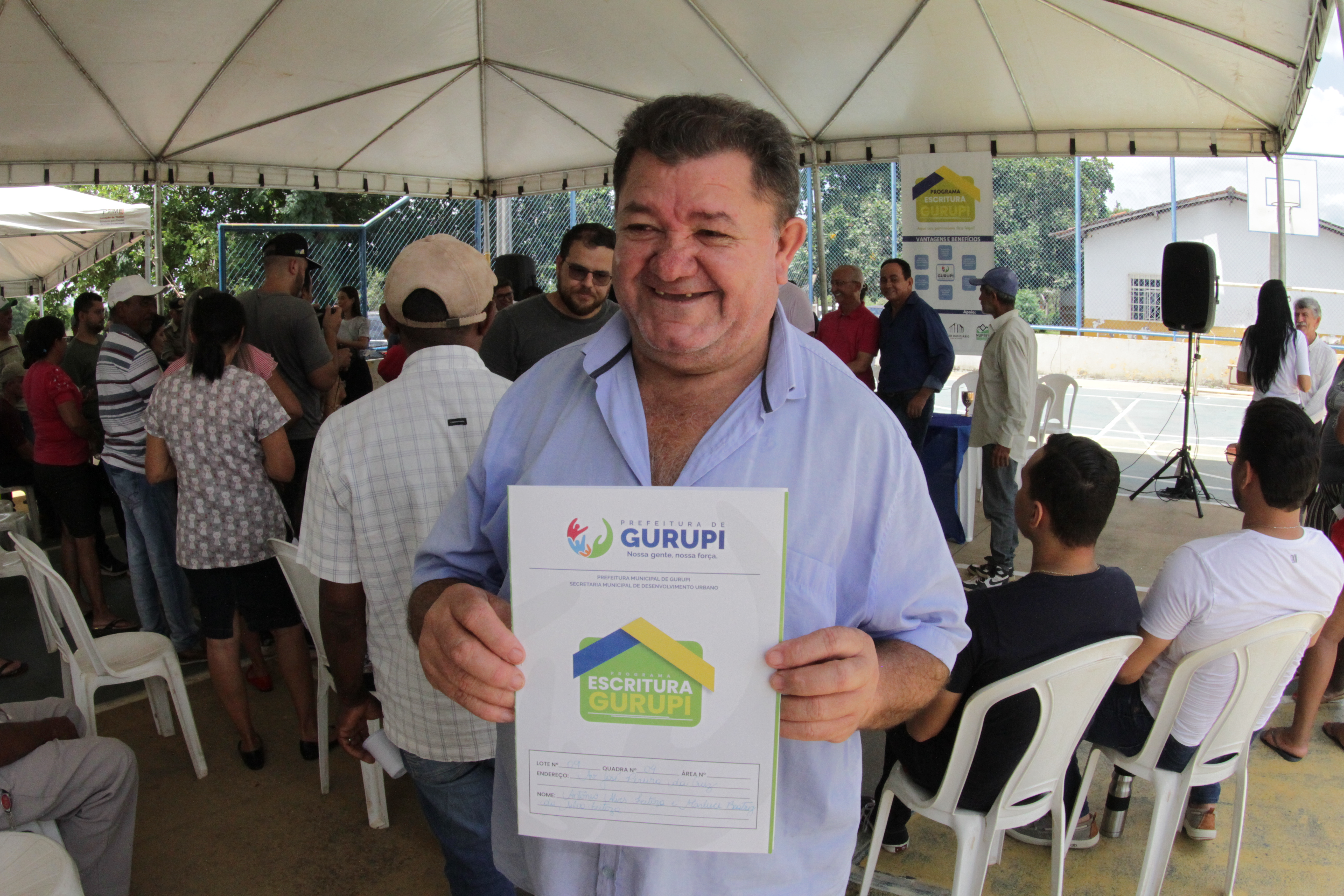 Fotografia colorida que mostras um homem branco sorrindo e segurando um documento de regularização fundiária