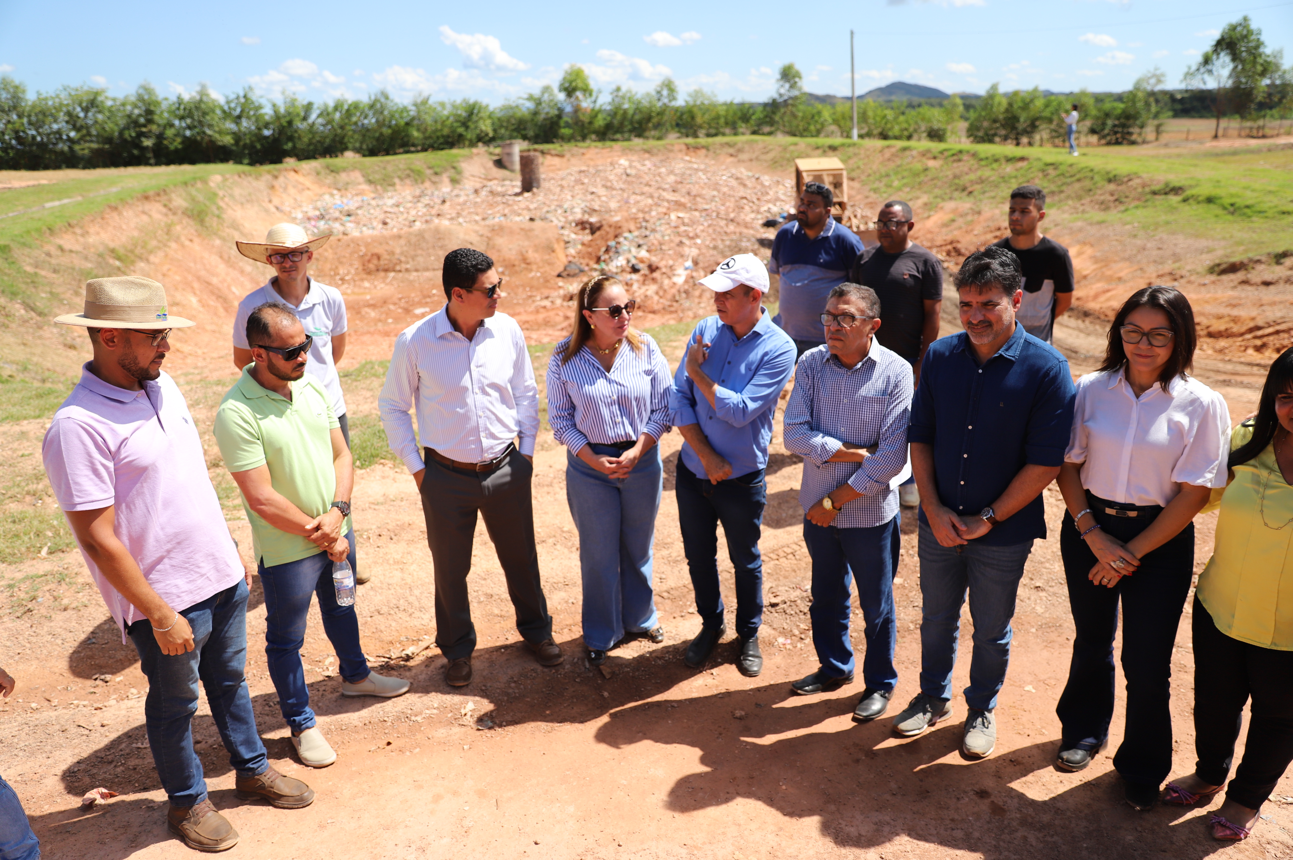 Imagem mostra várias pessoa sem pé em um terreno de terra e atrás um aterro sanitário