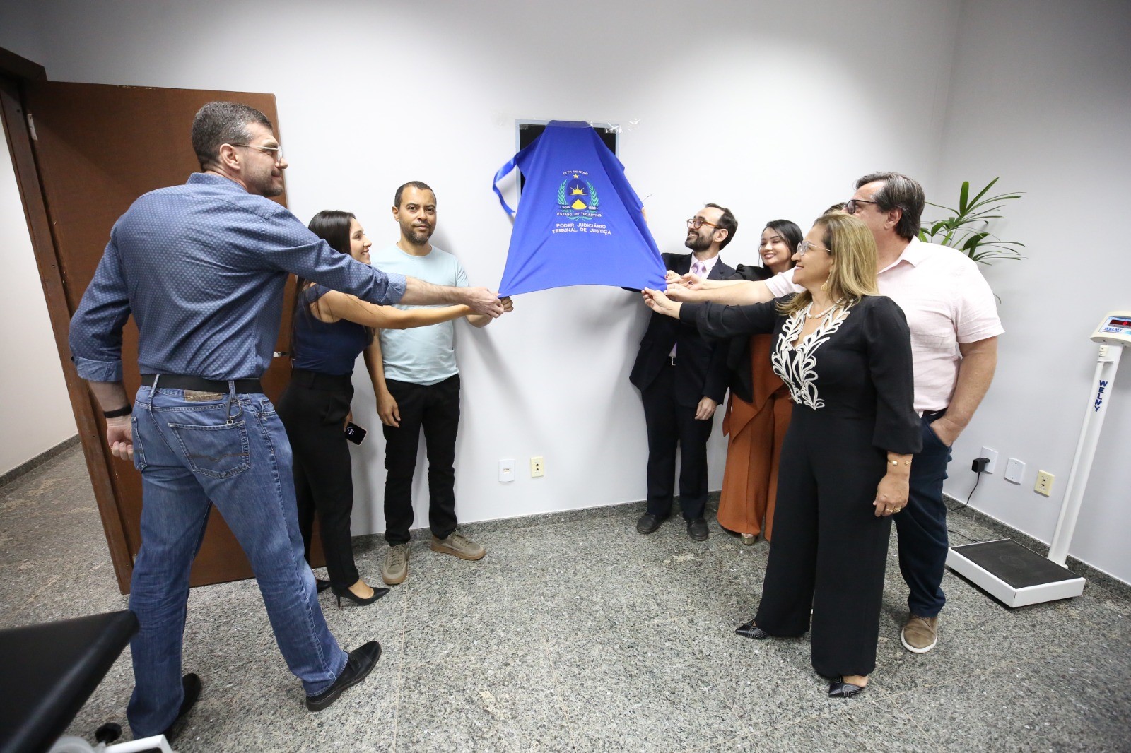 Grupo de oito pessoas segurando um pano azul que exibe logotipo e texto com os dizeres "Poder Judiciário Tribunal de Justiça".