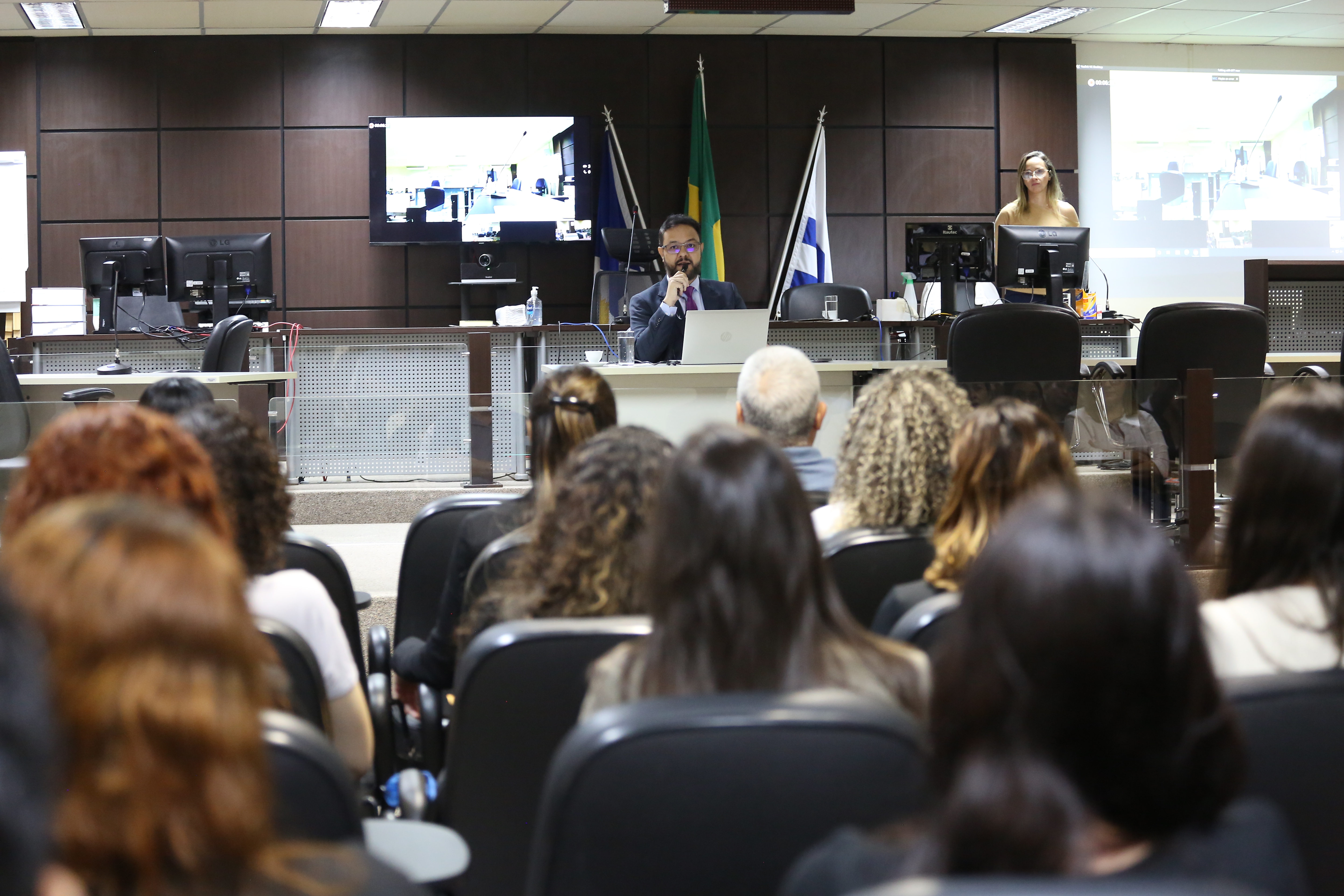 No Salão do Tribunal do Júri do Fórum de Palmas, o juiz Cledson Nunes, ao fundo, sentado, fala ao microfone para os jurados, que estão sentados de frente p ele e de costas para a foto no auditório.