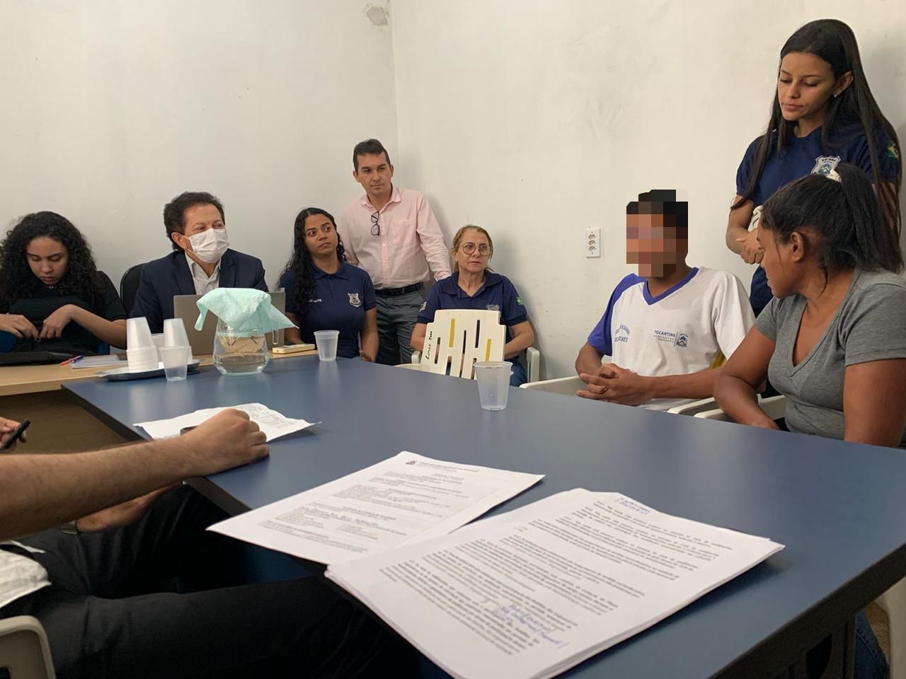 imagem aberta de uma das audiências realizadas em Araguaína; juiz aparece sentado, na cabeceira da mesa (ele usa máscara), e ao seu lado servidores, socioeducandos e familiares