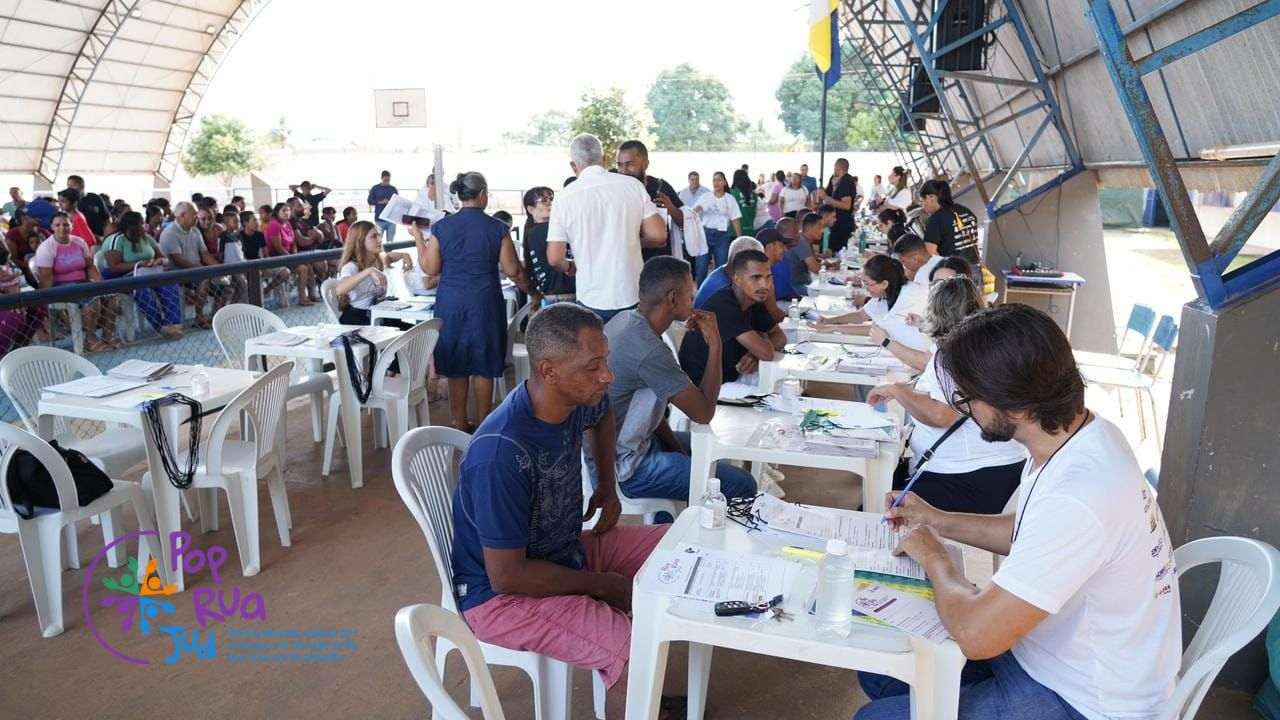 Imagem mostra pessoas sentadas em frente às mesas de triagem atendidas por voluntários do mutirão Pop Rua Jud