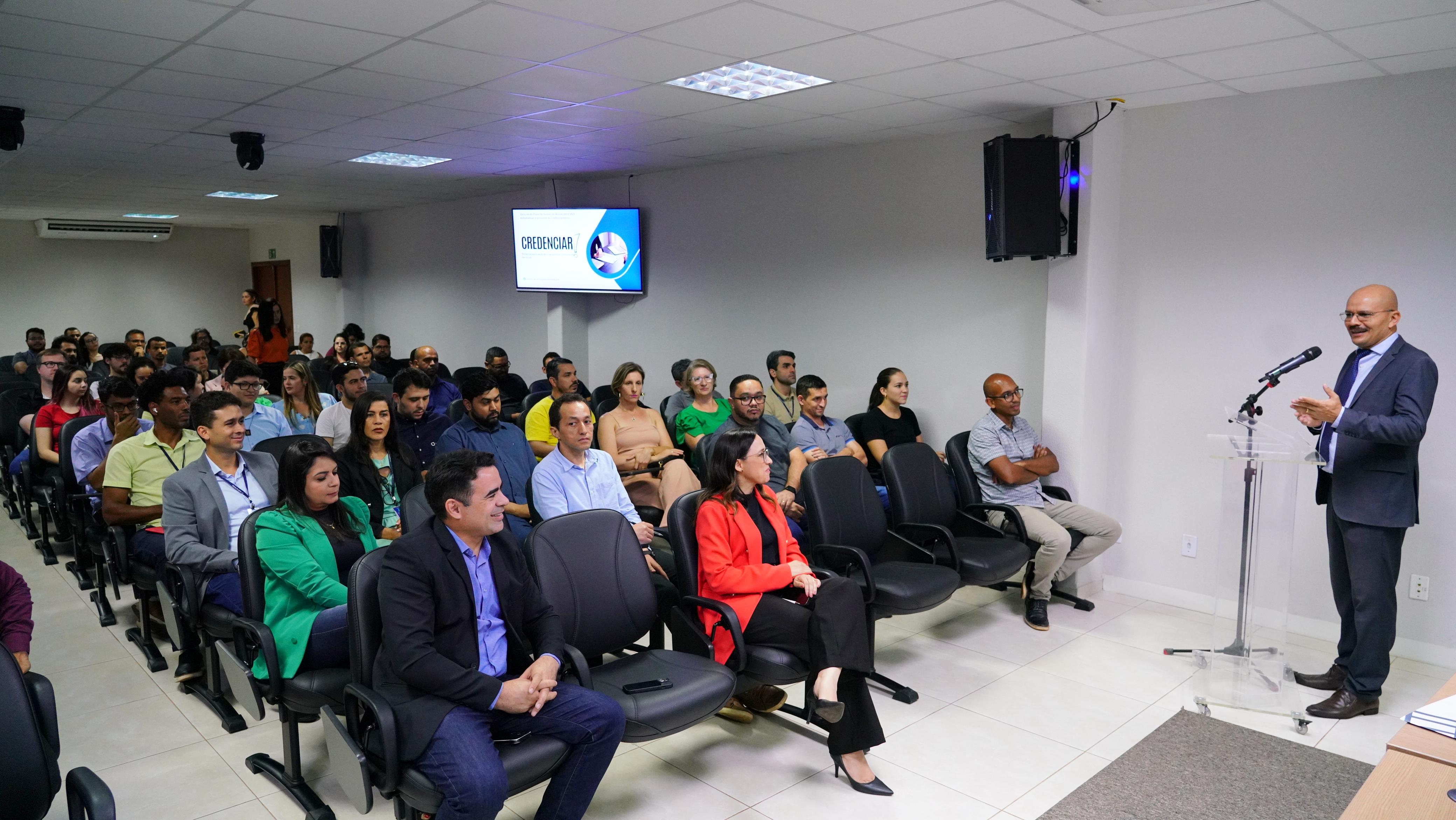 Grupo grande de pessoas sentadas e a frente, um mediador usando terno e gravata.