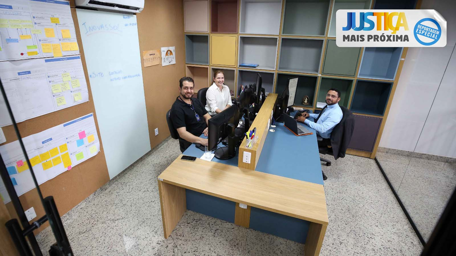 três servidores do Centro de Inovação do TJTO sentados na frente do computador na sala do Inovassol, na parte superior à direita, um selo com o nome Justiça Mais Próxima - Reportagem Especial