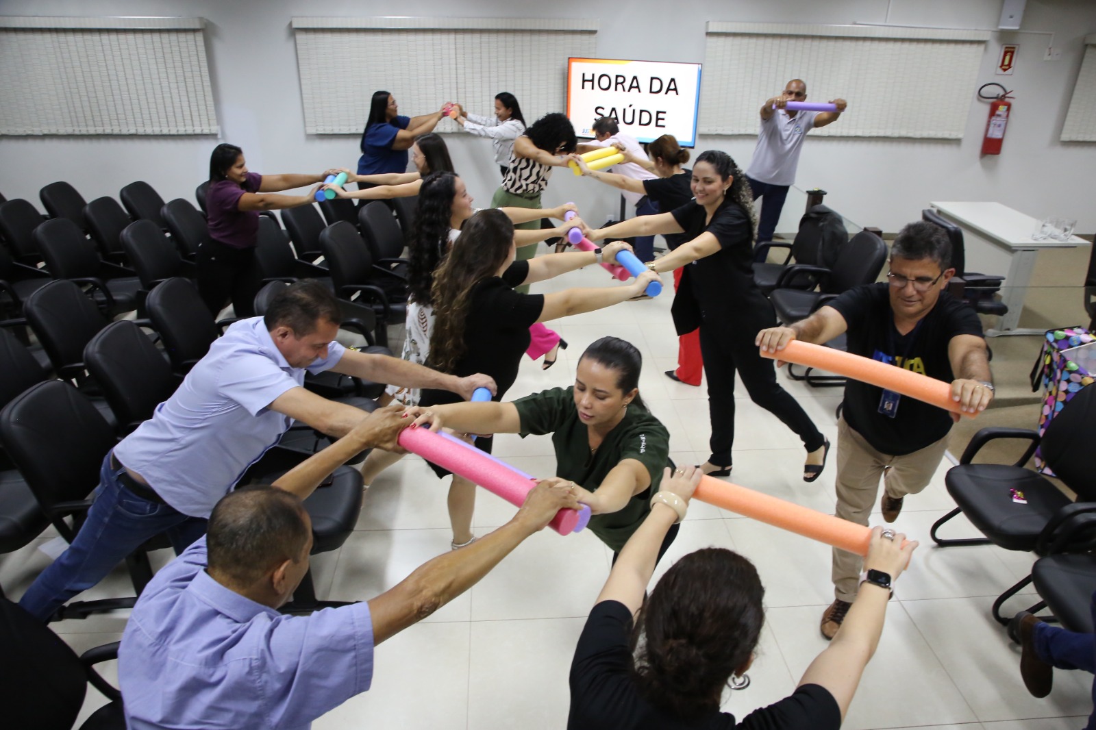 Vários servidores, numa sala, com macarrões de esponja nas mãos, praticando a ginástica laboral 