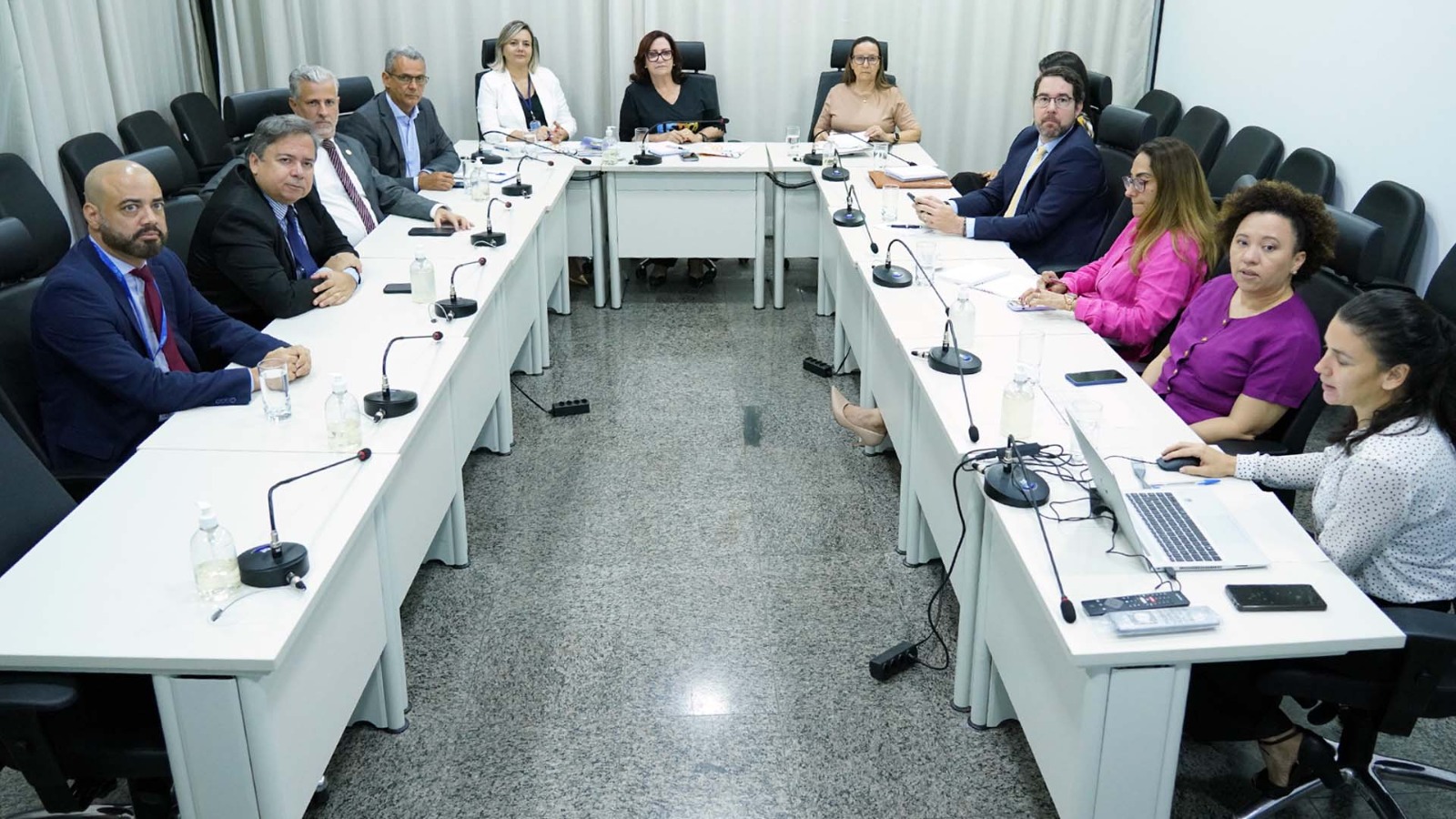 foto colorida horizontal mostra mulheres e homens sentados em uma mesa em formato u