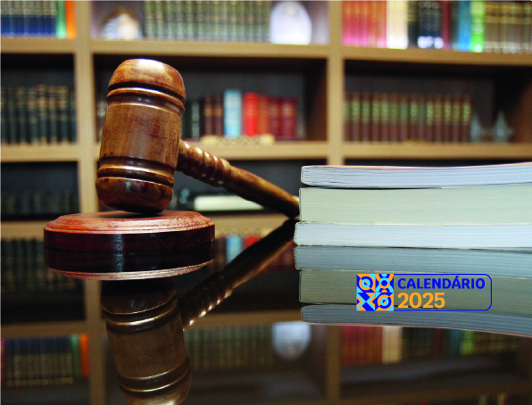 Foto mostra uma mesa de madeira escura, ao lado livros e um martelo de madeira