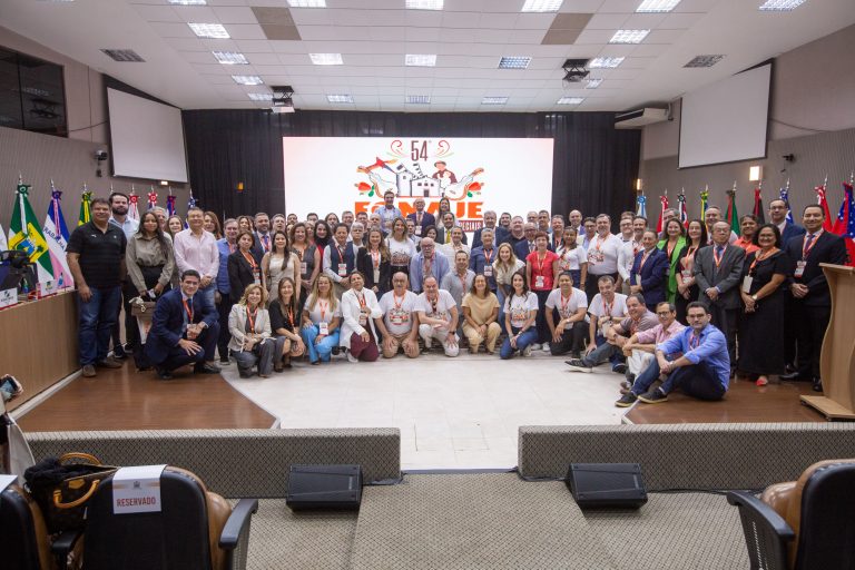 Homens e mulheres em pé em sala de paredes e teto brancos, posando para foto 