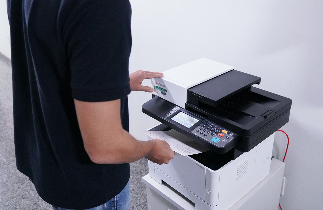 Imagem ilustrativa de uma pessoa do sexo masculino vestido de preto manuseando um equipamento de impressão