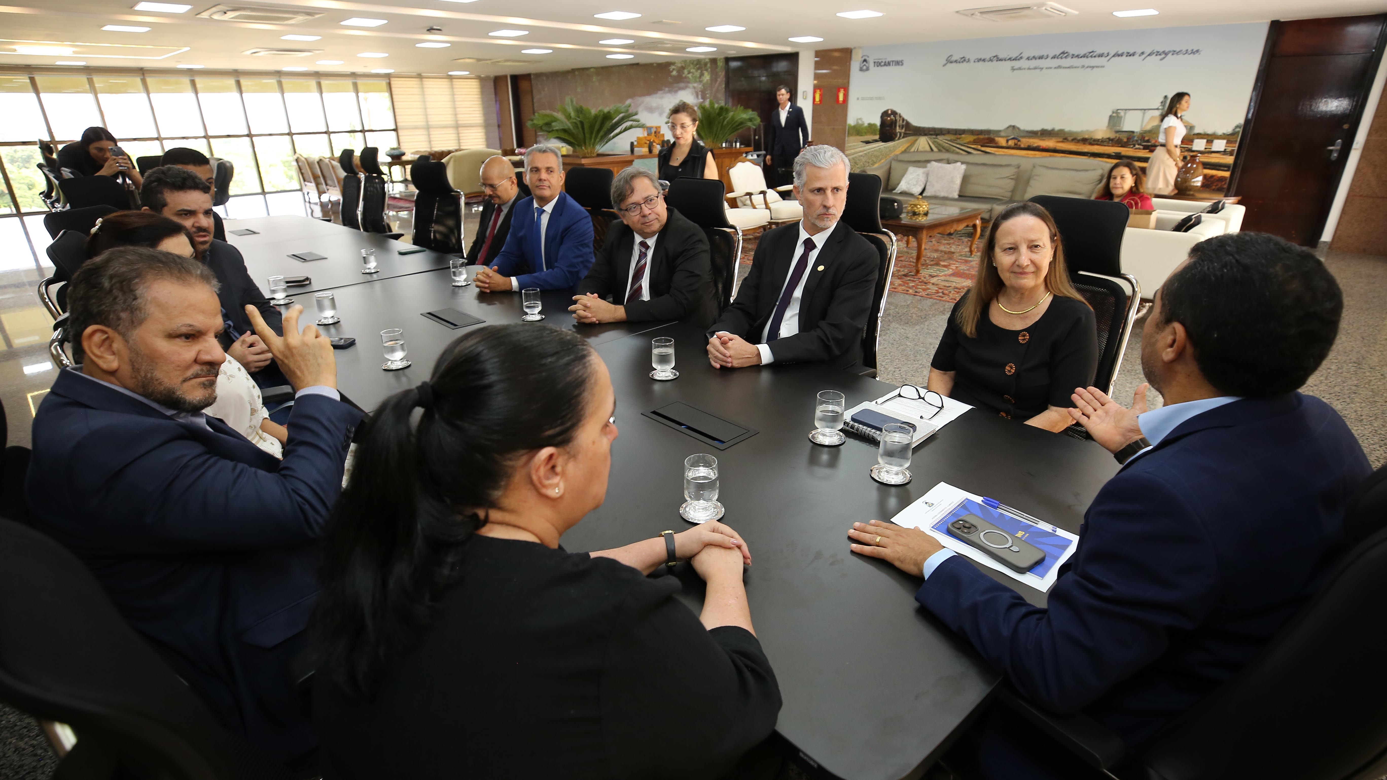 Foto aberta no gabinete do governador do Tocantins onde estão sentados à mesa, em reunião, o governador Wanderlei Barbosa (de costa), a desembargadora Maysa, magistrados, diretores do TJTO e secretários