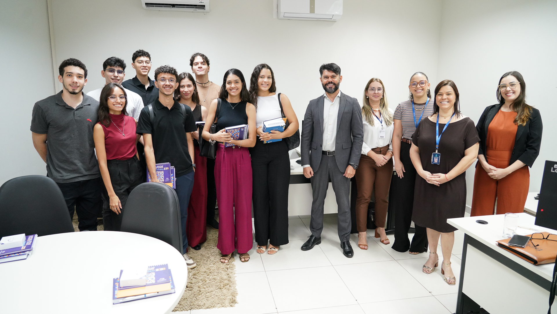 A fotografia mostra um grupo de pessoas em pé posando sorrindo em uma sala do Nacom.