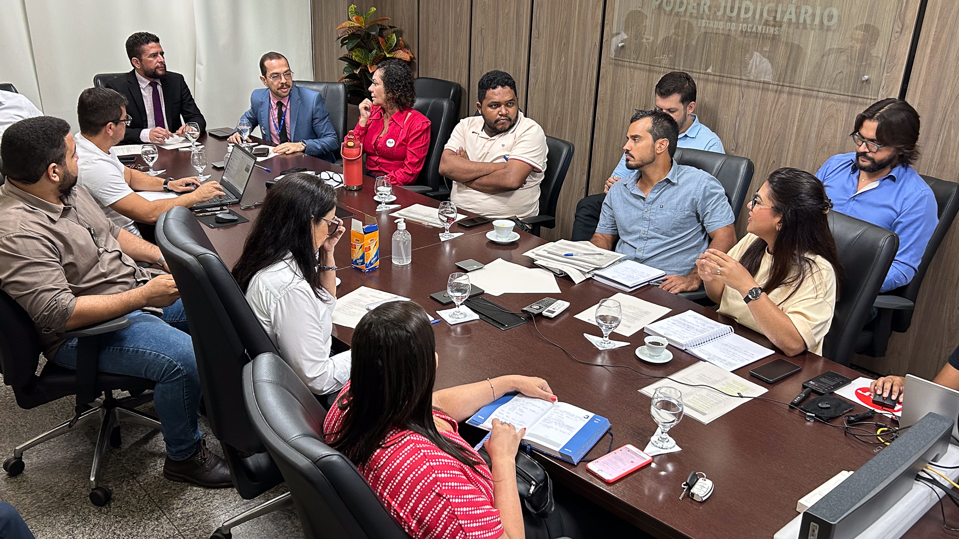 Foto aberta com várias pessoas sentadas em volta de uma mesa em reunião