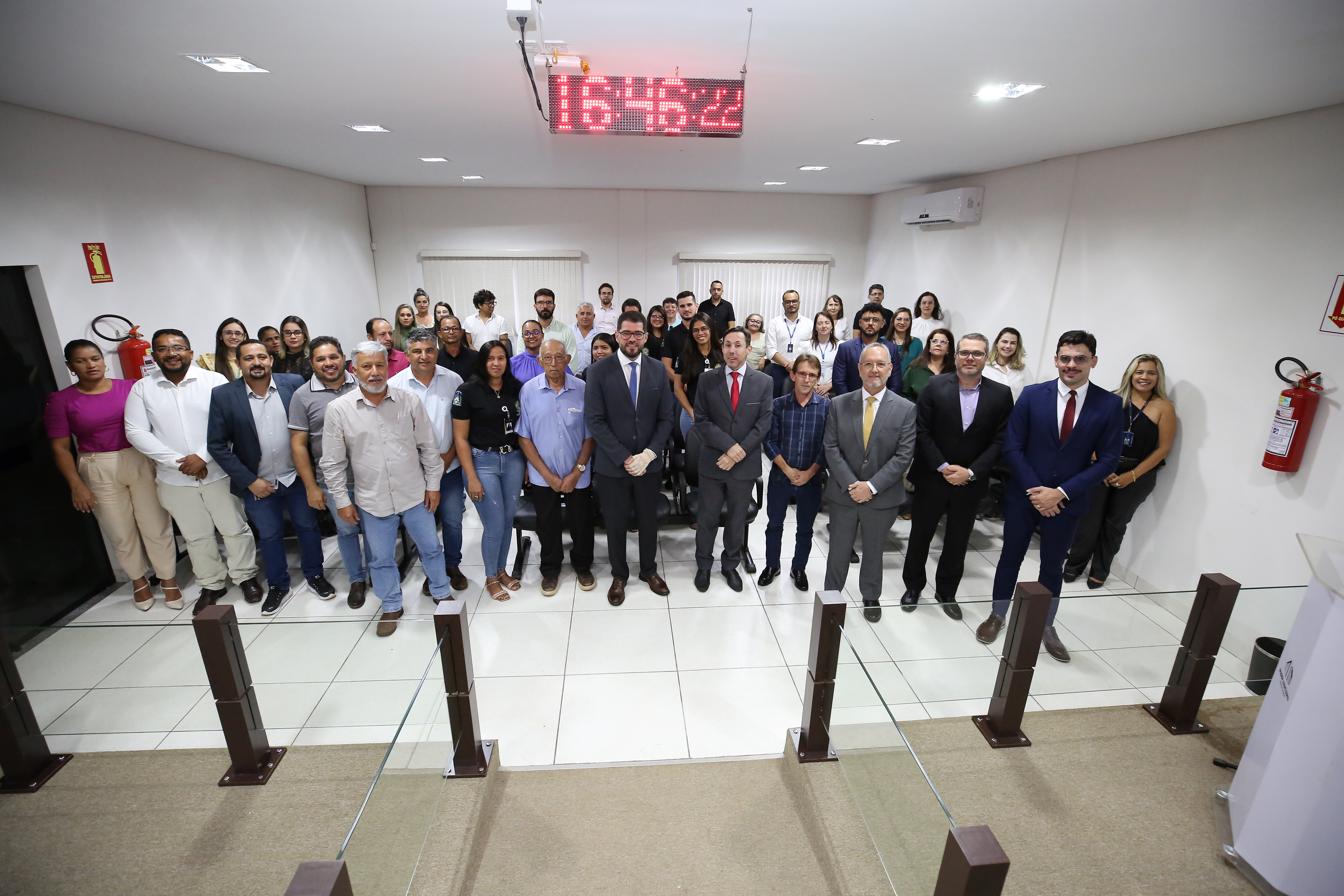 Homens e mulheres em pé em foto posada em sala de paredes brancas