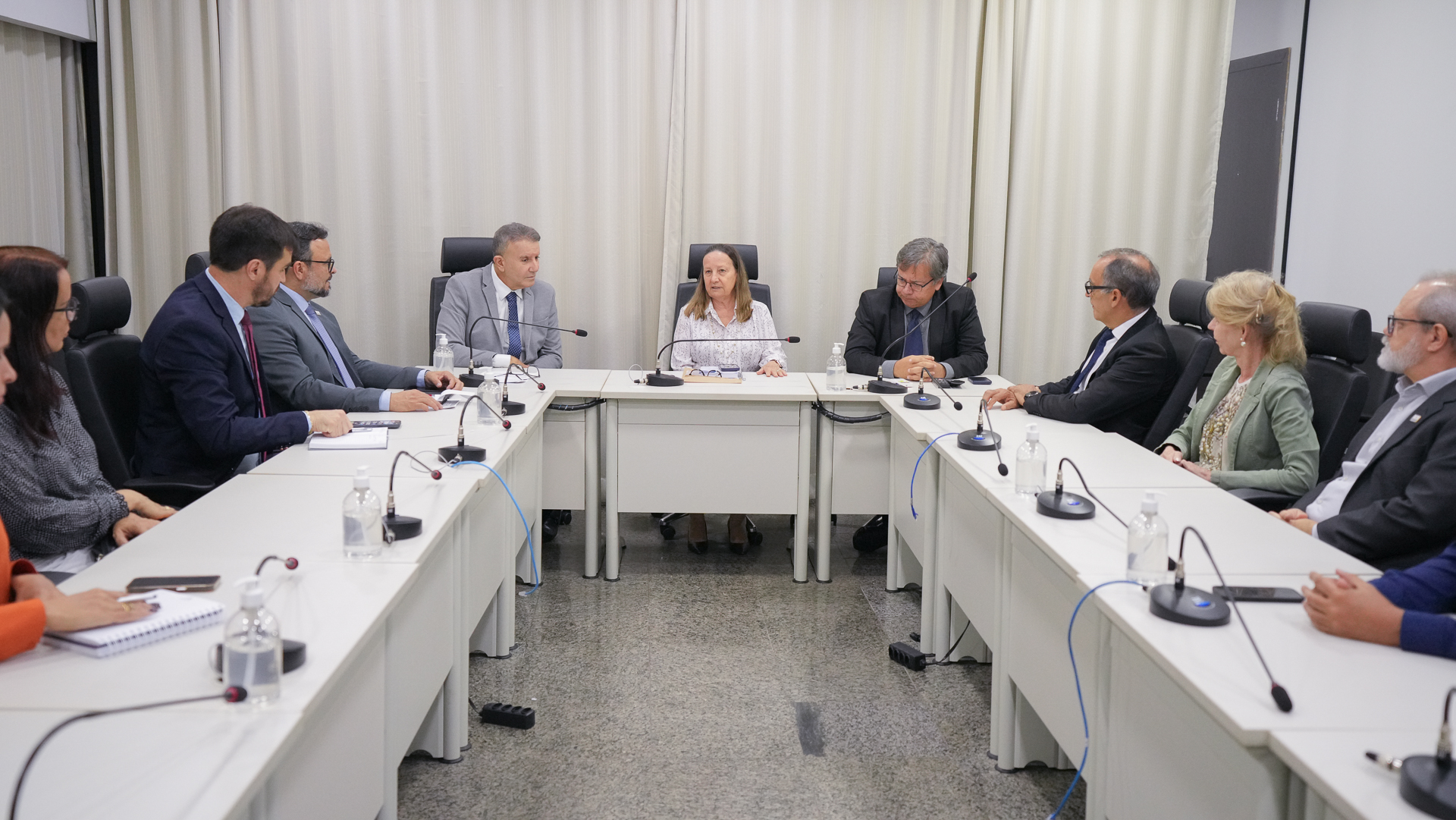  Imagem mostra a presidente do TJTO ao centro, ao lado de autoridades e de magistrados reunidos, sentados em torno de uma grande mesa de reuniões em forma de "U", discutindo a organização do Refis 2025.