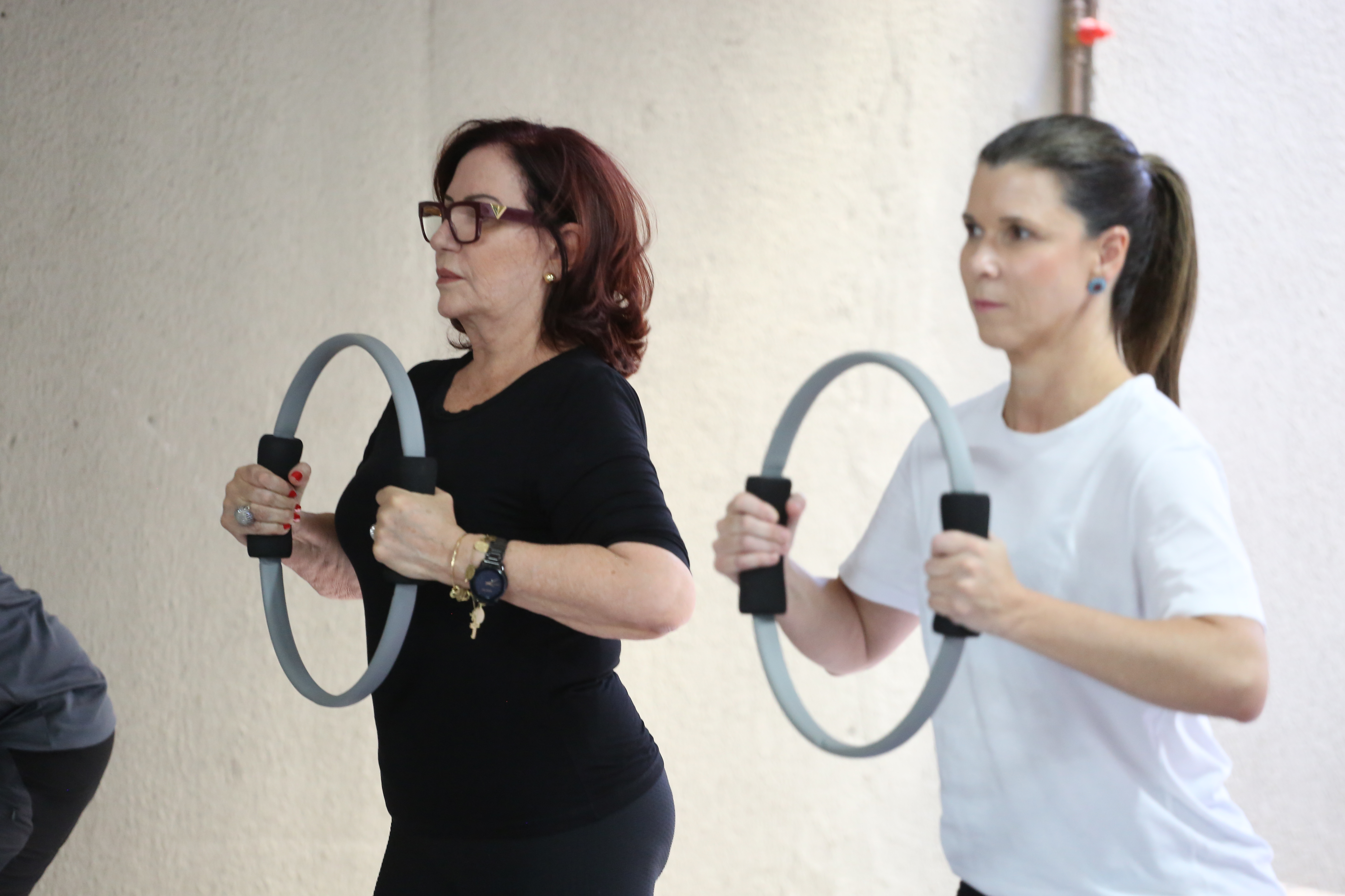 Desembargadora Etelvina, de roupa preta, à esquerda, e a médica Elaine, de branco, à direita, se exercitando com uma argola nas mãos