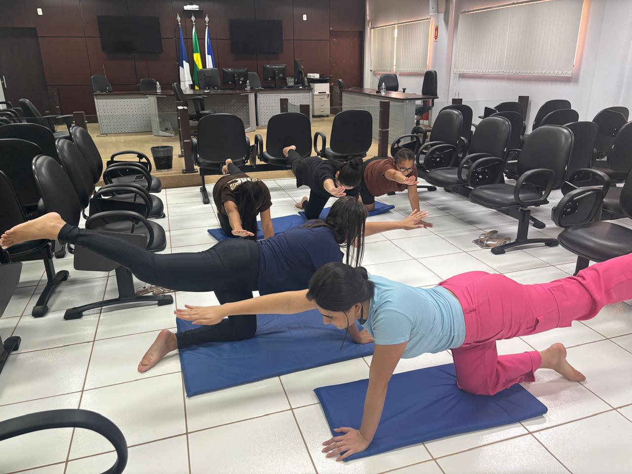 Sala com vários servidores se exercitando em tapetes azuis