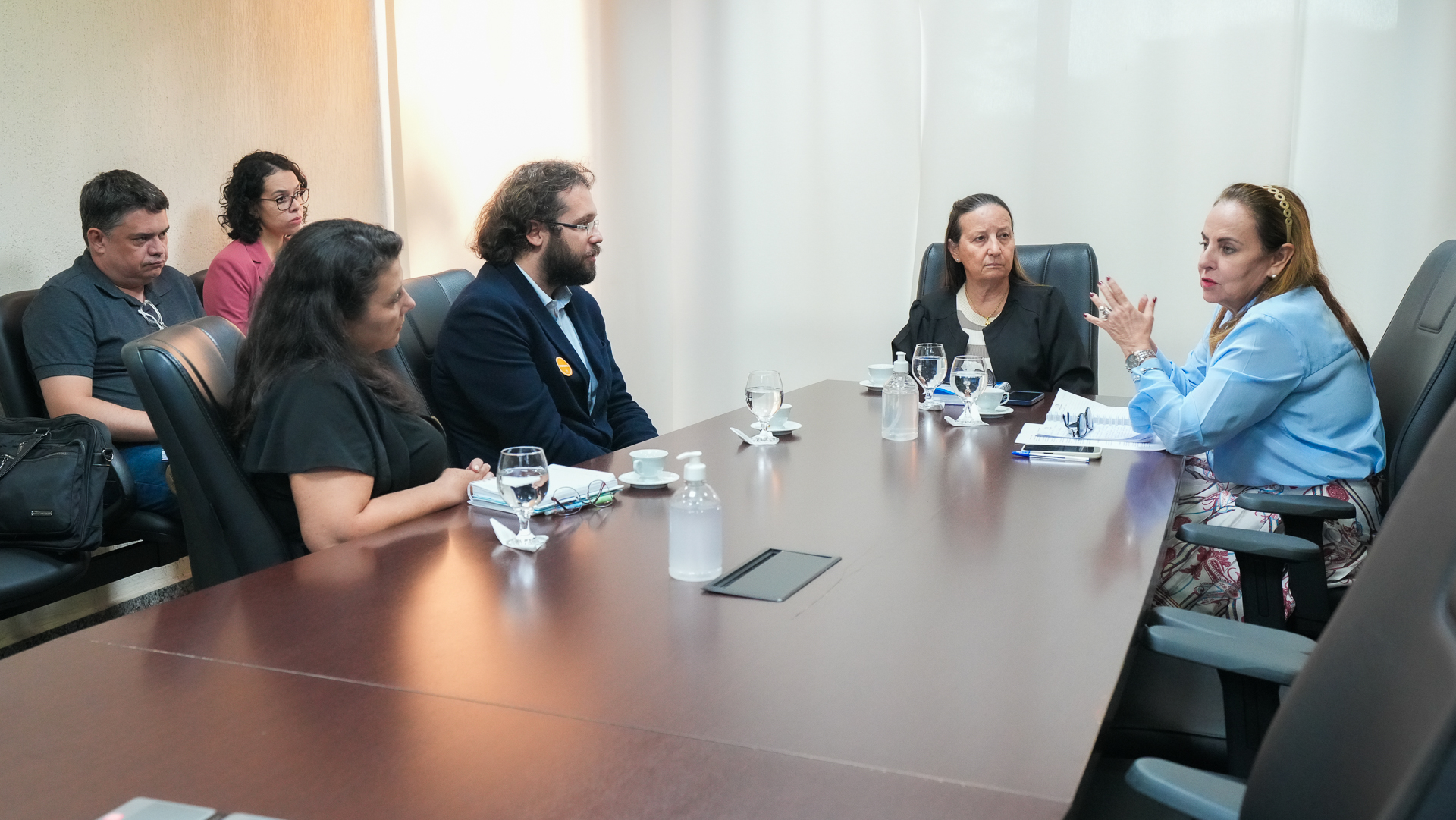 Imagem de uma reunião em torno de uma mesa, com várias pessoas sentadas e conversando