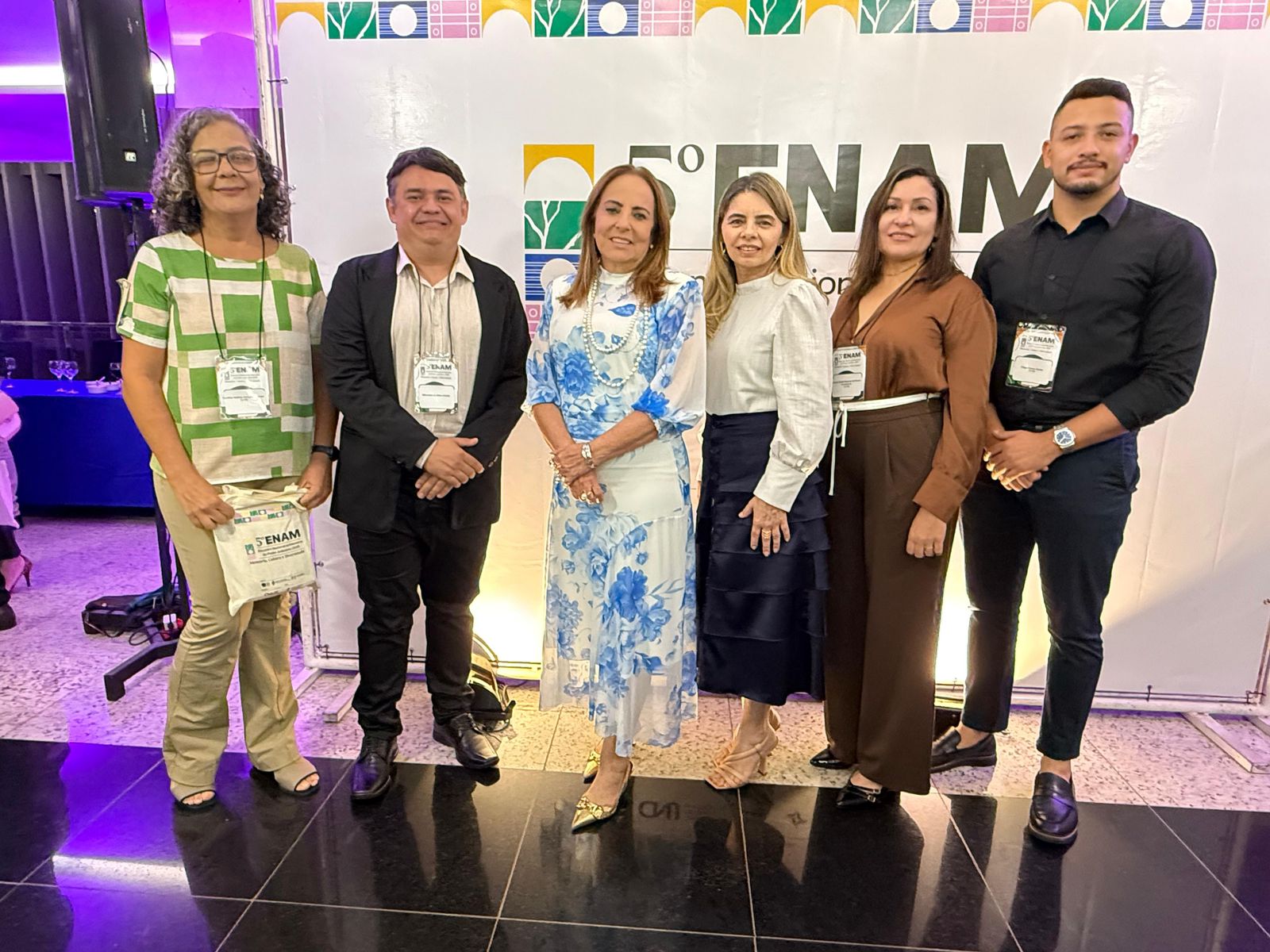 Cinco pessoas, ao centro a desembargadora Ângela Prudente, posando para uma foto em um evento, vestindo roupas casuais e formais.