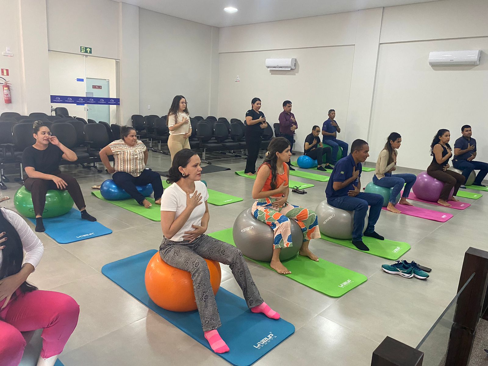Várias pessoas em uma sala se exercitando com tapetes e bolas coloridas