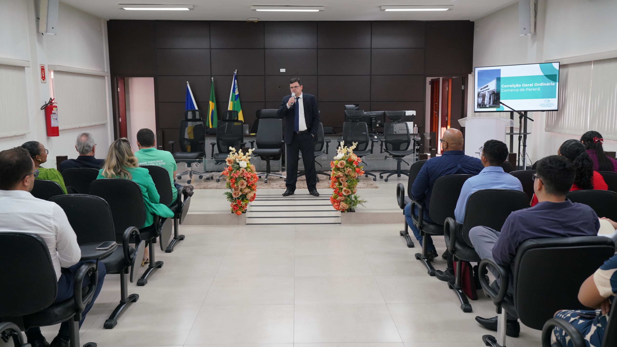 Auditório com muitas pessoas sentadas, assistindo o juiz Frederico falar ao microfone no palco