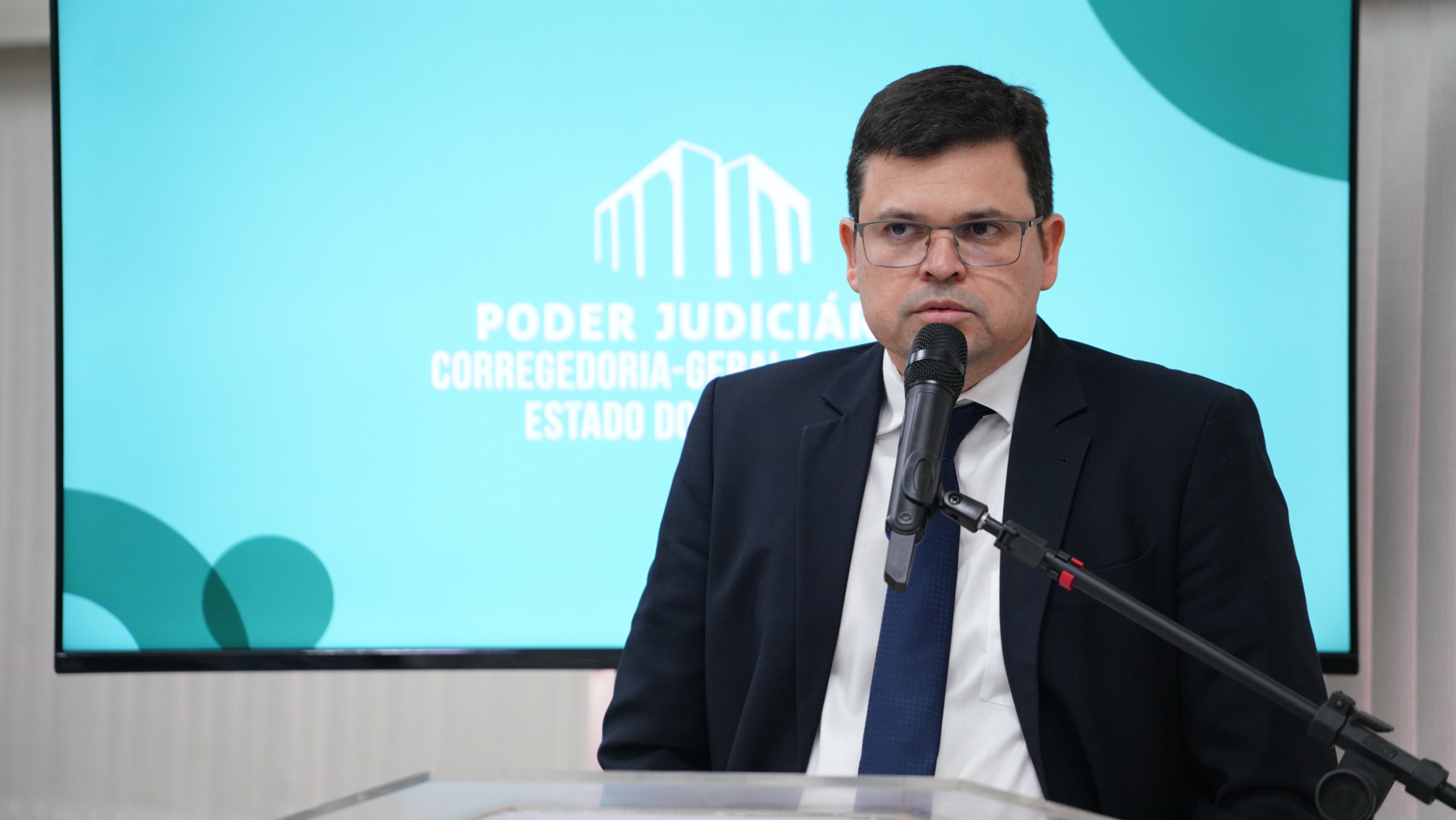 Juiz Frederico Paiva, homem de pele clara, usando terno e gravata escuros e camisa branca, fala ao microfone