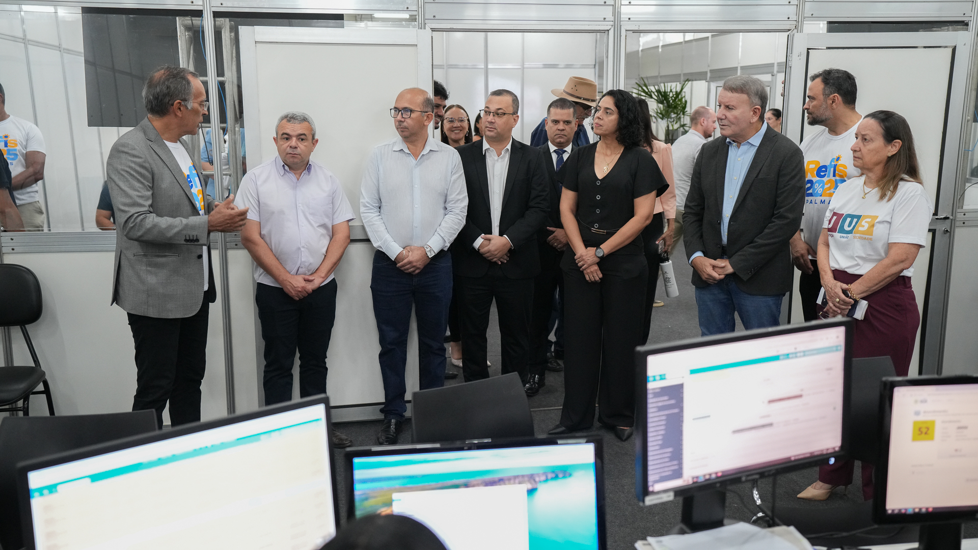 Na imagem aparecem cerca de 10 pessoas reunidas em uma sala iluminada. Além das pessoas aparecem também computadores. Elas estão na estrutura, onde está sendo realizada a 6ª edição do Refis, em Palmas.