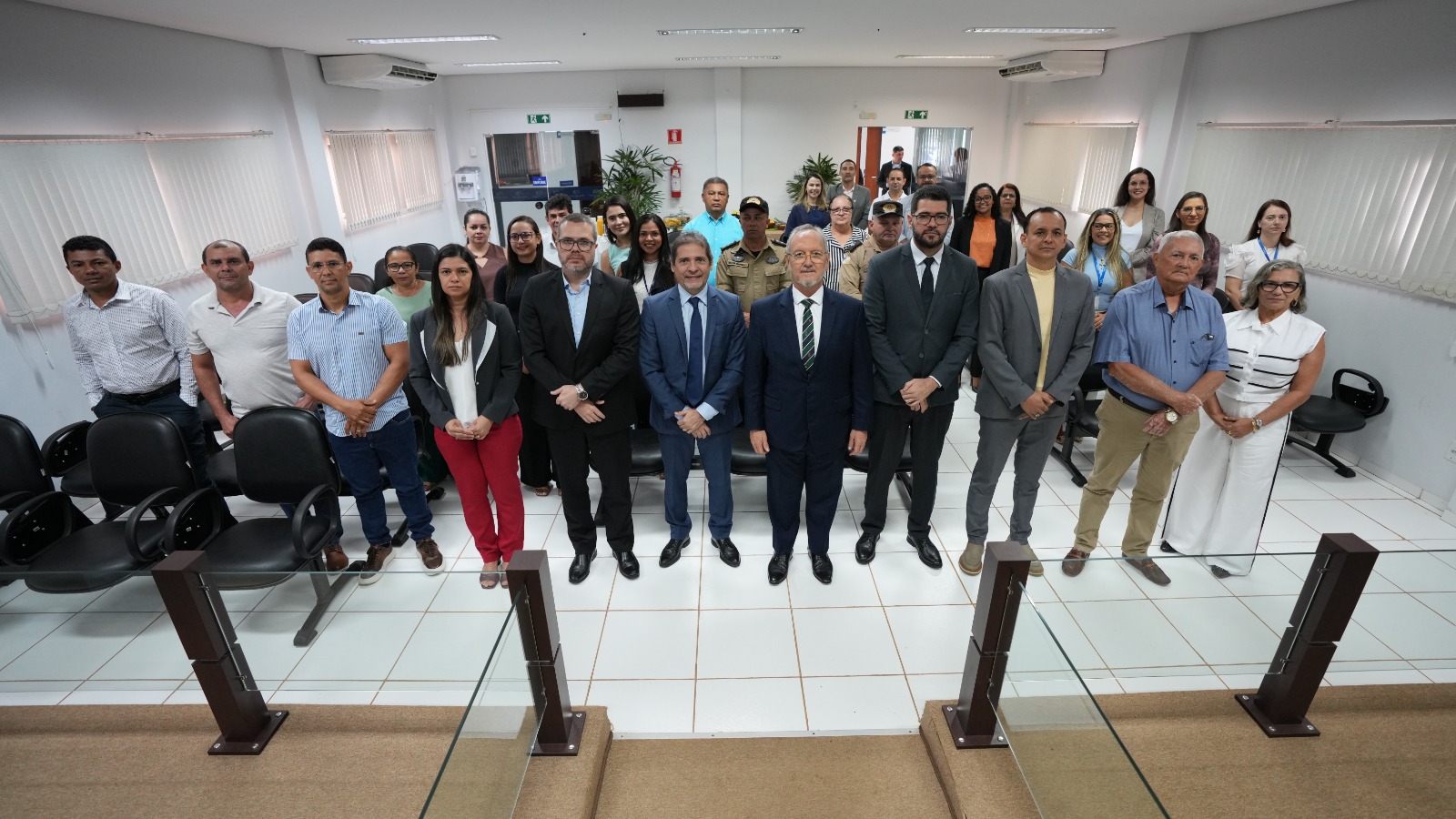 A imagem mostra um grupo de pessoas em pé, organizadas em várias fileiras, posicionadas em frente a um piso de cor clara. Elas participam da Correição Geral Ordinária da Comarca de Goiatins. Os participantes estão vestidos com roupas formais, com predominância de cores como azul, cinza e bege.