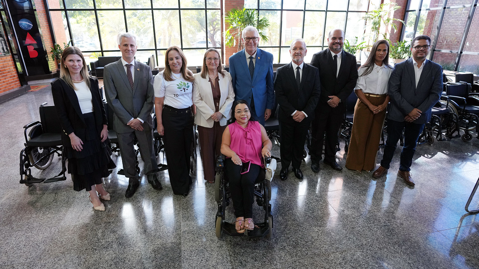 A imagem mostra um grupo de autoridades posando para a foto, com várias cadeiras de rodas alinhadas ao fundo. As cadeiras de rodas foram doadas pelo Tribunal de Justiça à Secretaria de Saúde do Tocantins.