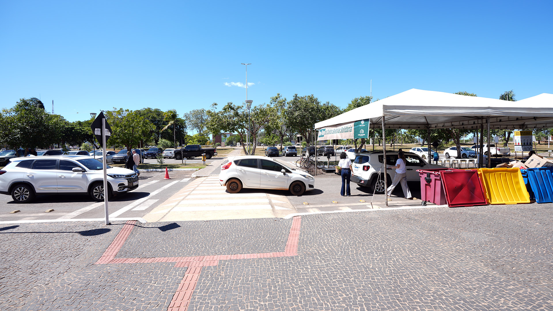 Carros passando por estrutura montada em estacionamento como ponto de descarte de material reciclável