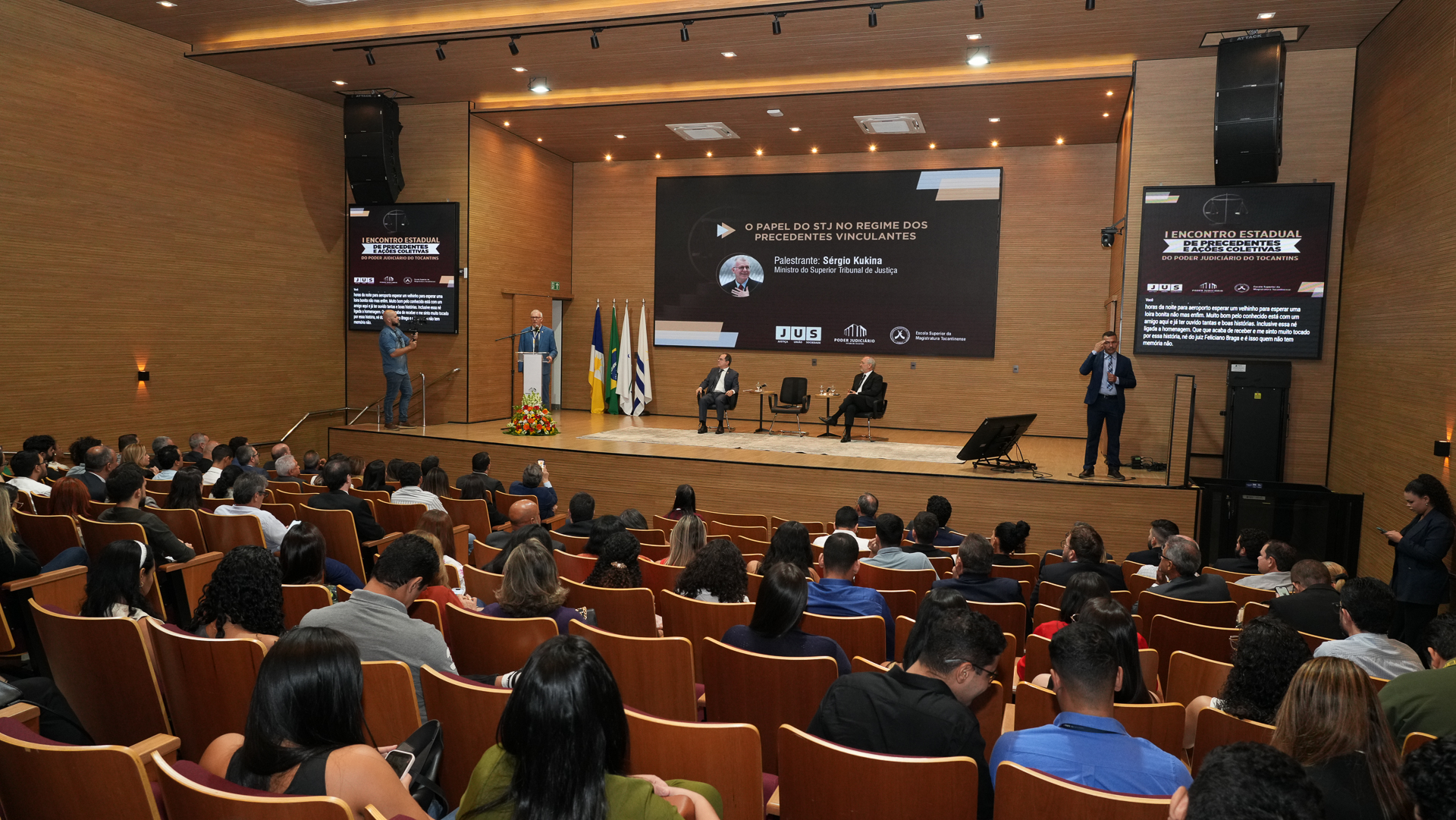 Imagem aberta do auditório mostrando o público sentado, assistindo a palestra do ministro, que fala no pauco ao fundo