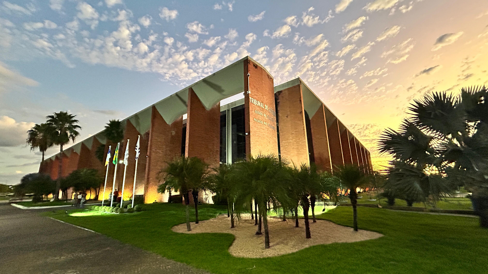 Fachada do prédio do Tribunal de Justiça do Tocantins; com seus carcos de concreto e revestimento cerâmico; à frente jardim com grama e palmeiras 