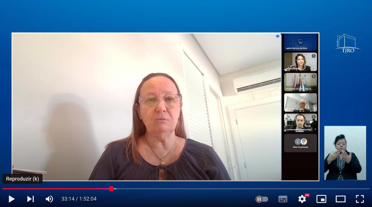 Pessoa assiste, pelo notebook, à transmissão de uma audiência pública virtual. Na tela, aparece a presidente do Tribunal de Justiça do Tocantins, desembargadora Maysa Vendramini Rosal, usando blusa escura e óculos, falando de um ambiente claro com paredes brancas. A transmissão exibe o título “Elaboração das Metas Nacionais do Poder Judiciário para 2026” e a faixa inferior da tela indica: “Audiência Pública – Justiça Estadual da Região Norte”, acompanhada do logotipo do TJTO. Sobre a mesa, ao lado do notebook, estão uma xícara, cadernos e uma caneta.