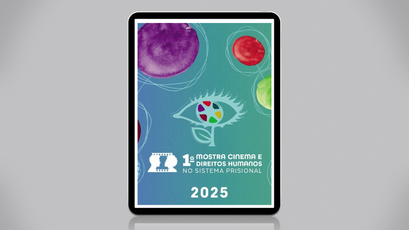 Imagem de um tablet exibindo o cartaz da "1ª Mostra Cinema e Direitos Humanos no Sistema Prisional – 2025". O fundo é colorido com tons suaves e formas aquareladas. Ao centro, há um desenho de um olho com íris colorida e, abaixo, o nome do evento em letras brancas.