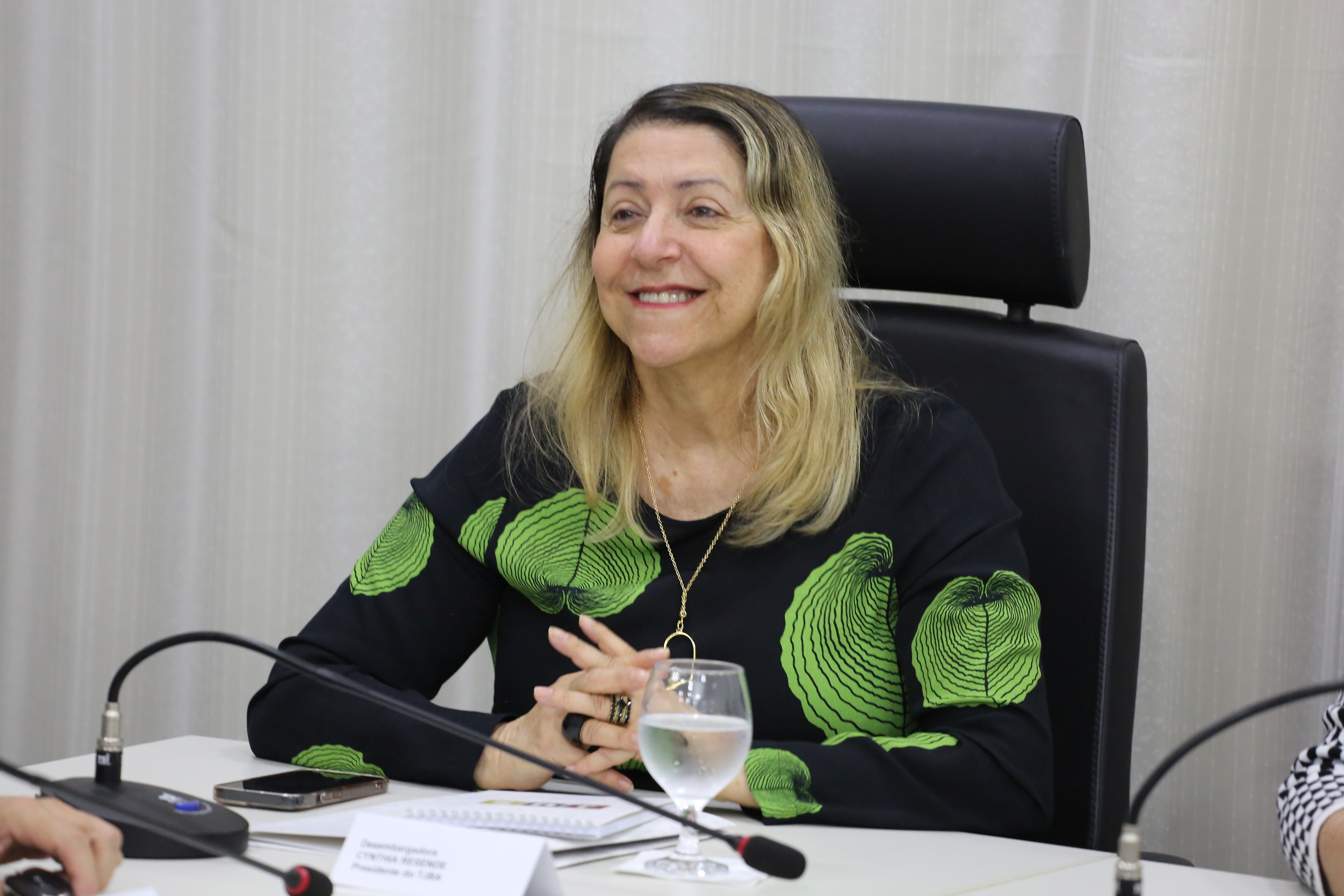 Presidente do TJBA, mulher de pele branca e cabelos louros; ela usa roupa estampada nas cores preta e verde