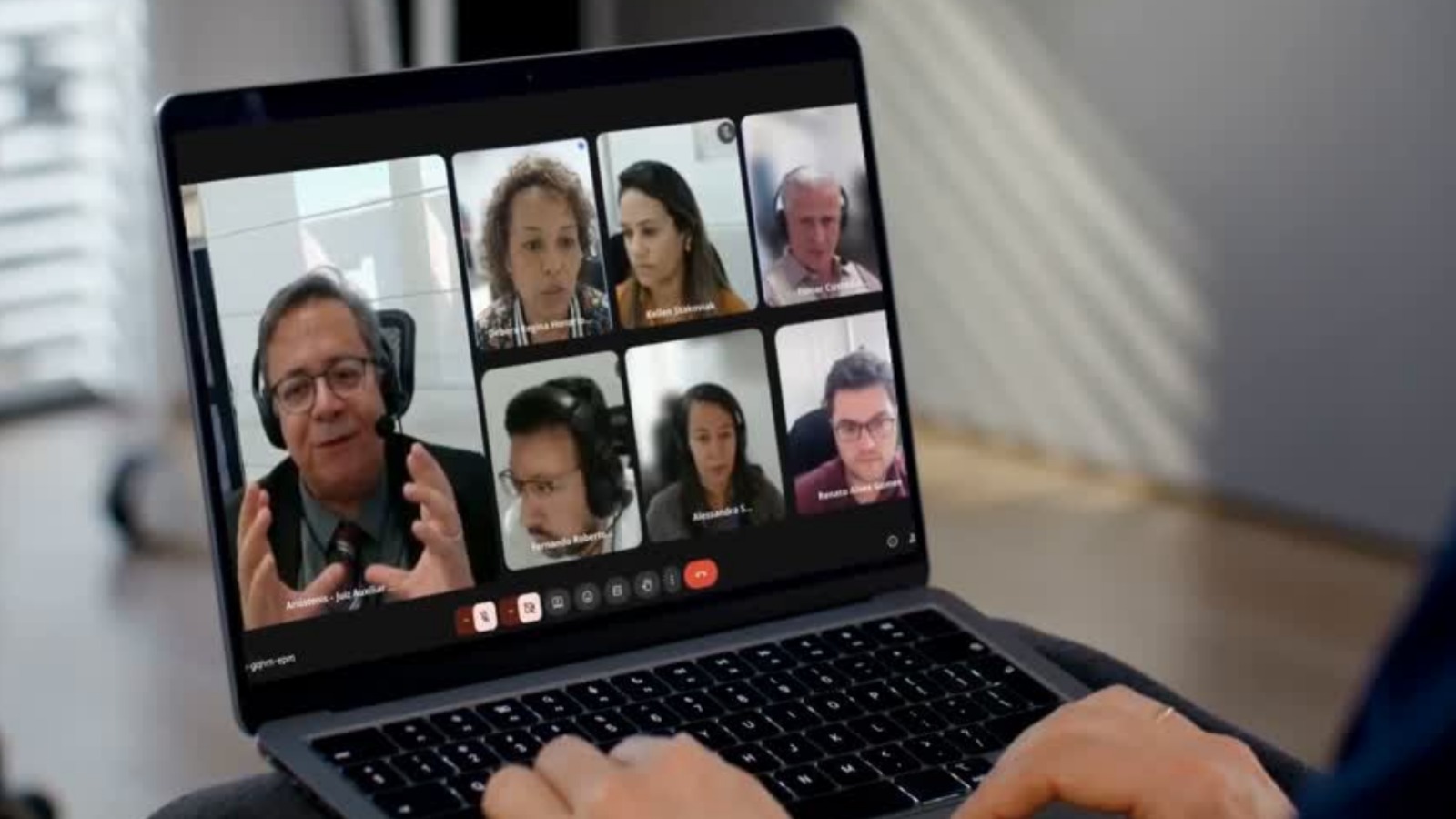 A imagem mostra a tela de um notebook com sete participantes atentos, todos envolvidos em uma reunião colaborativa para debater sugestões às Metas Nacionais do Judiciário 2026. Em destaque, um homem aparece gesticulando enquanto fala.