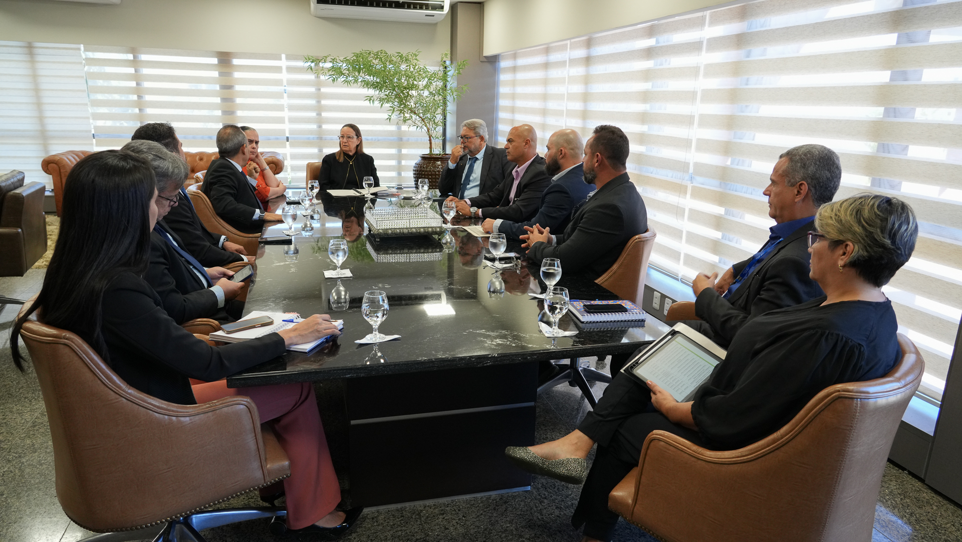 A imagem mostra representantes dos Poderes Judiciário e Executivo reunidos na sala de reuniões do TJTO, durante a entrega oficial do Plano Estadual 'Pena Justa' à presidente do Tribunal de Justiça do Tocantins. As autoridades estão sentadas ao redor de uma mesa retangular, acompanhando a apresentação do documento.