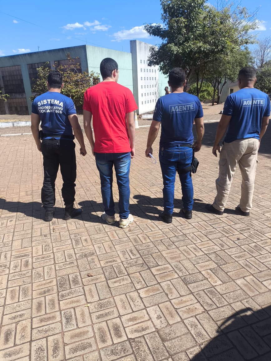 Jovel ao lado de três agentes, em pé, de costa, em frente ao prédio da universidade