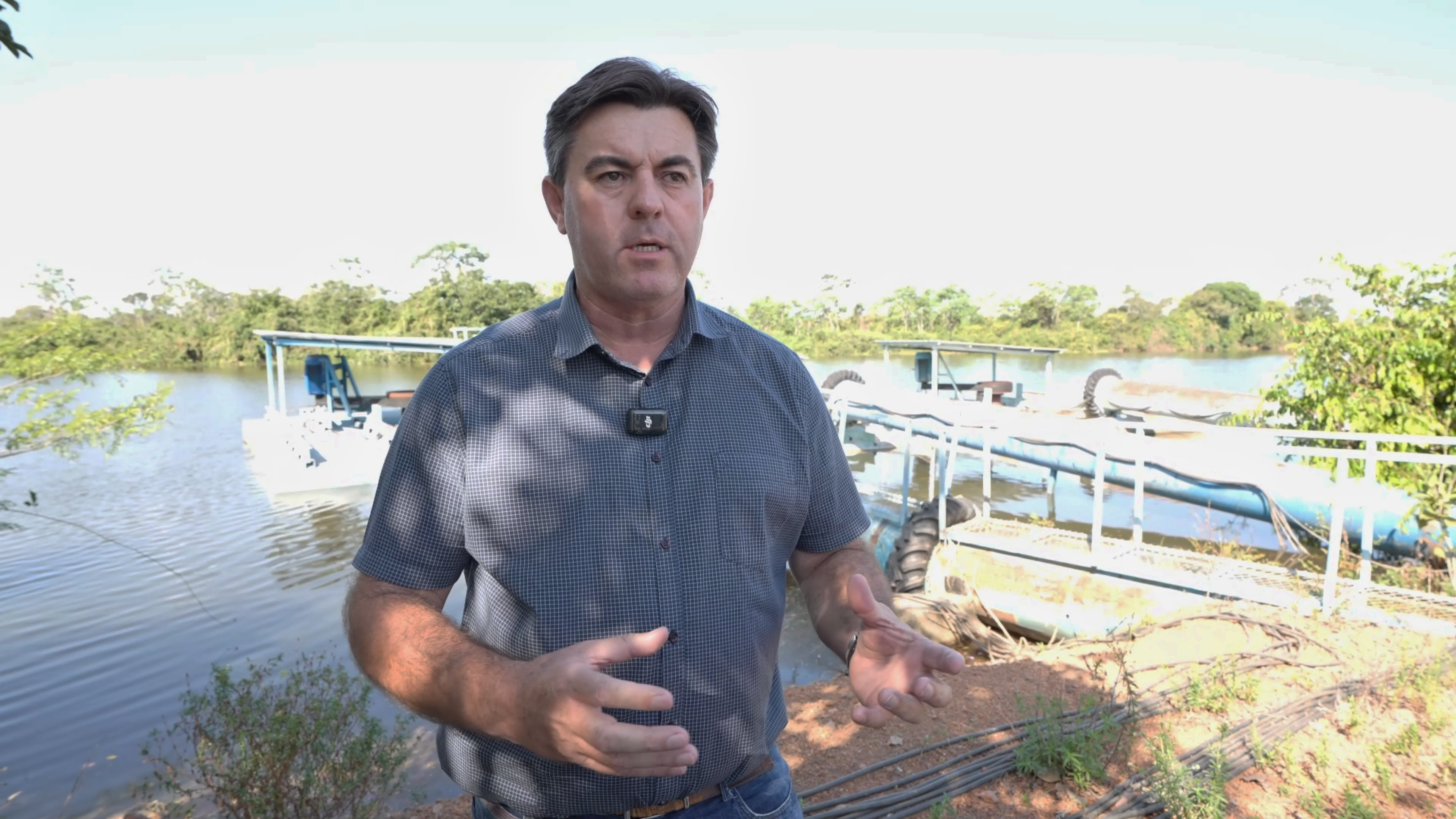 Produtor Josney, homem branco, cabelos lisos e escuros; ele usa camisa cinza e está falando em frente a uma barragem